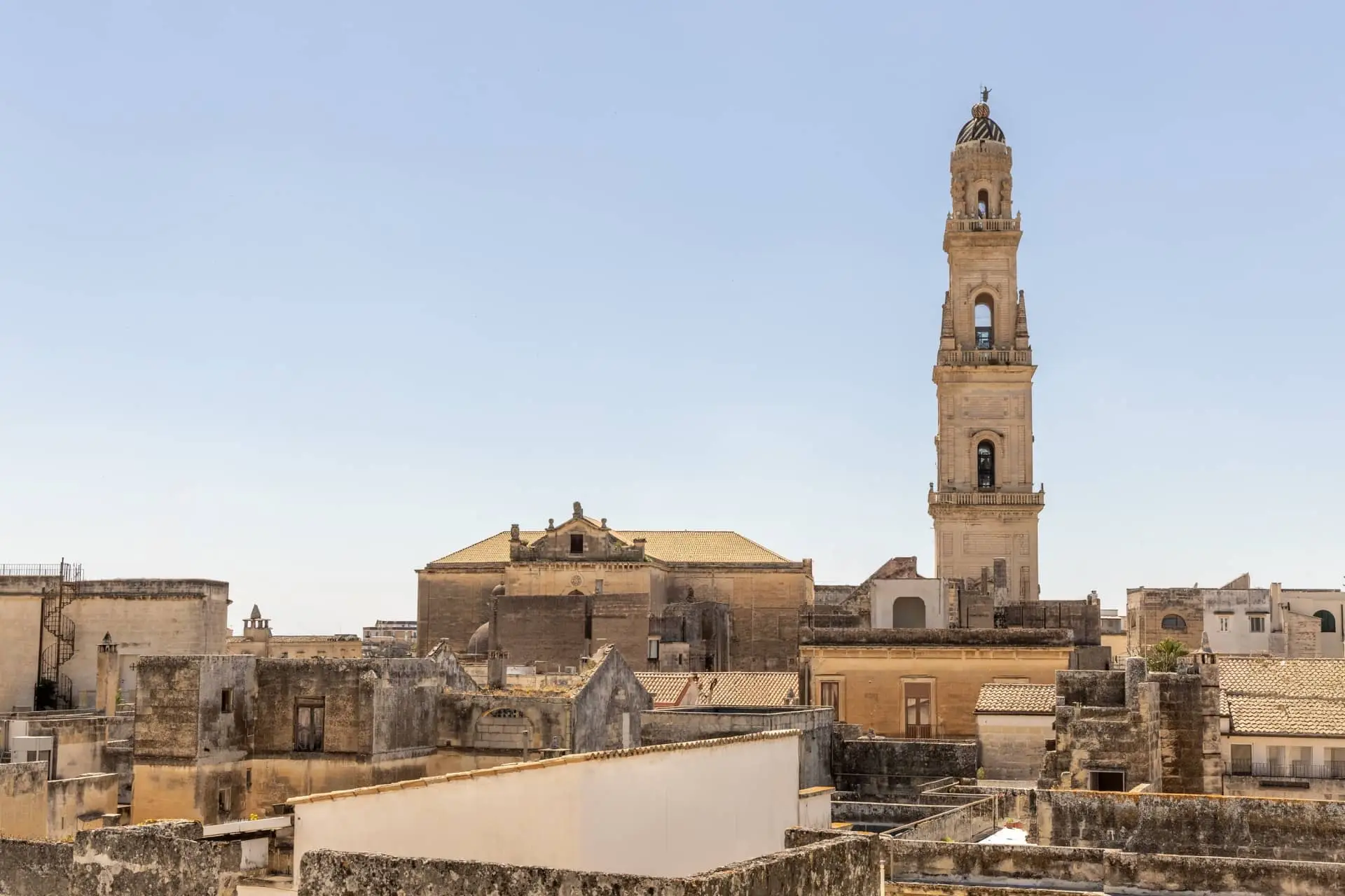 Historic city skyline with a tall clock tower against a pale sky at golden hour