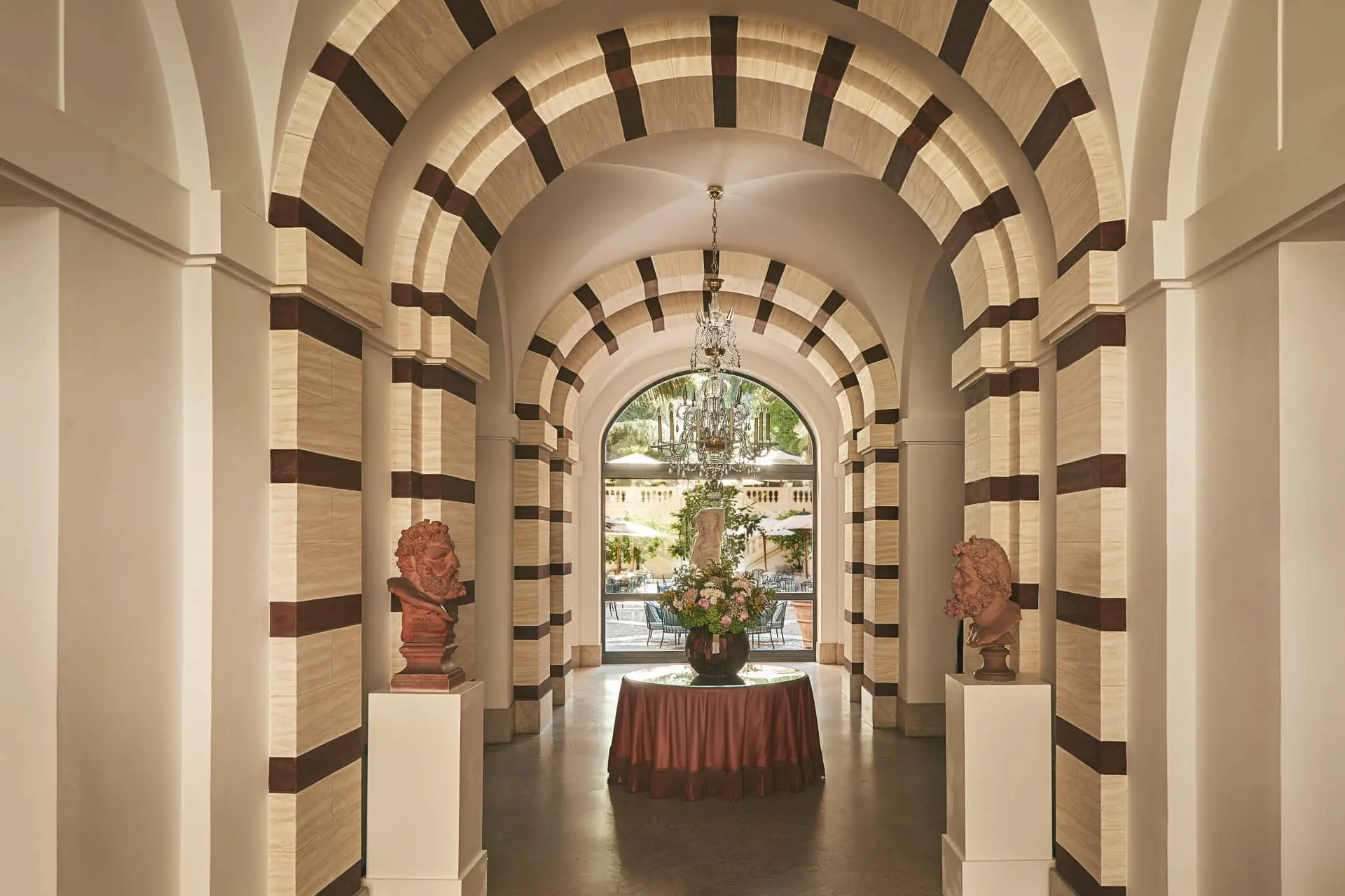 Cinematic hotel corridor with striped arches, hanging chandelier, and a set table at the end