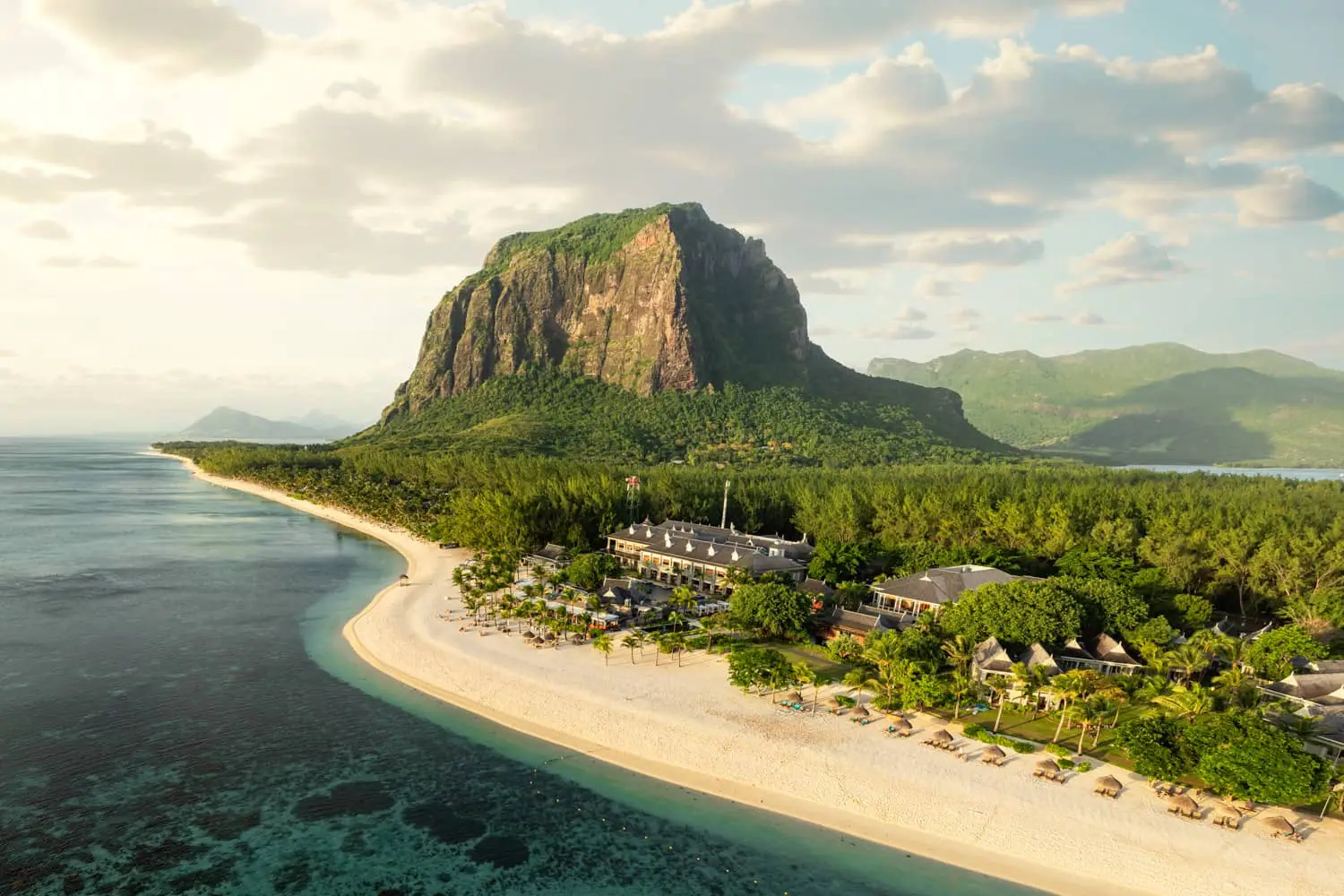 Tropical beachfront resort with a dramatic green headland and calm ocean at golden hour