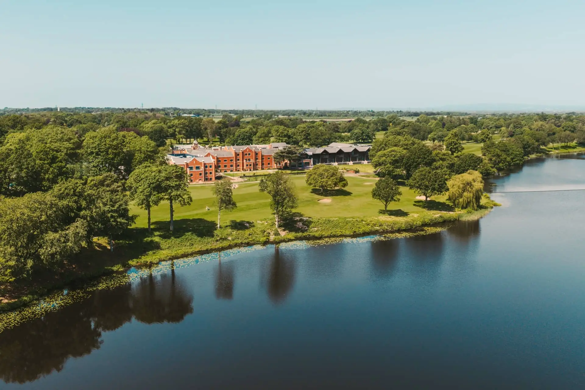 Aerial view of a luxury resort building beside a calm lake and landscaped gardens