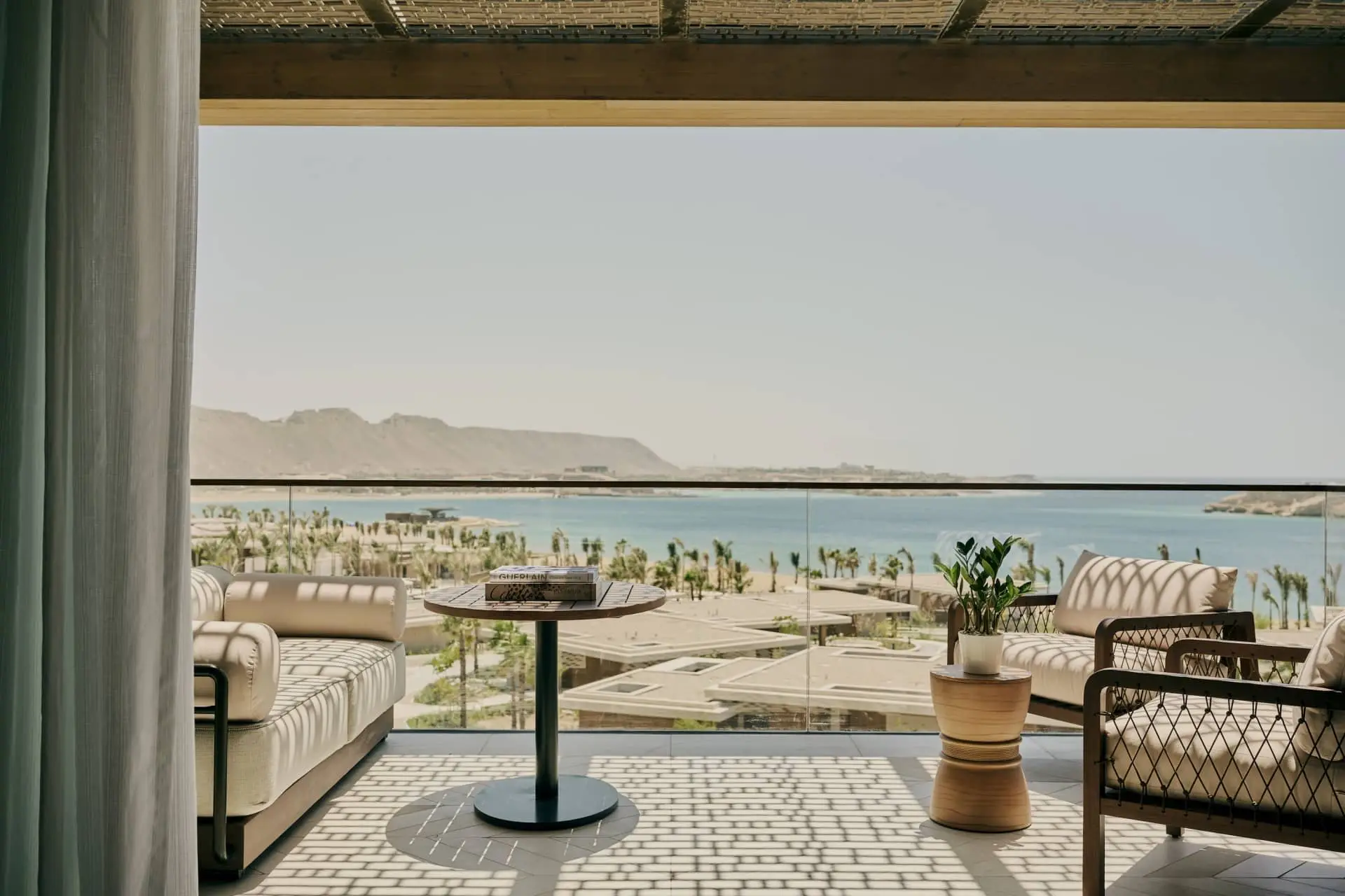 Luxury terrace lounge area with wicker seating, round table, potted plants, and ocean view beyond