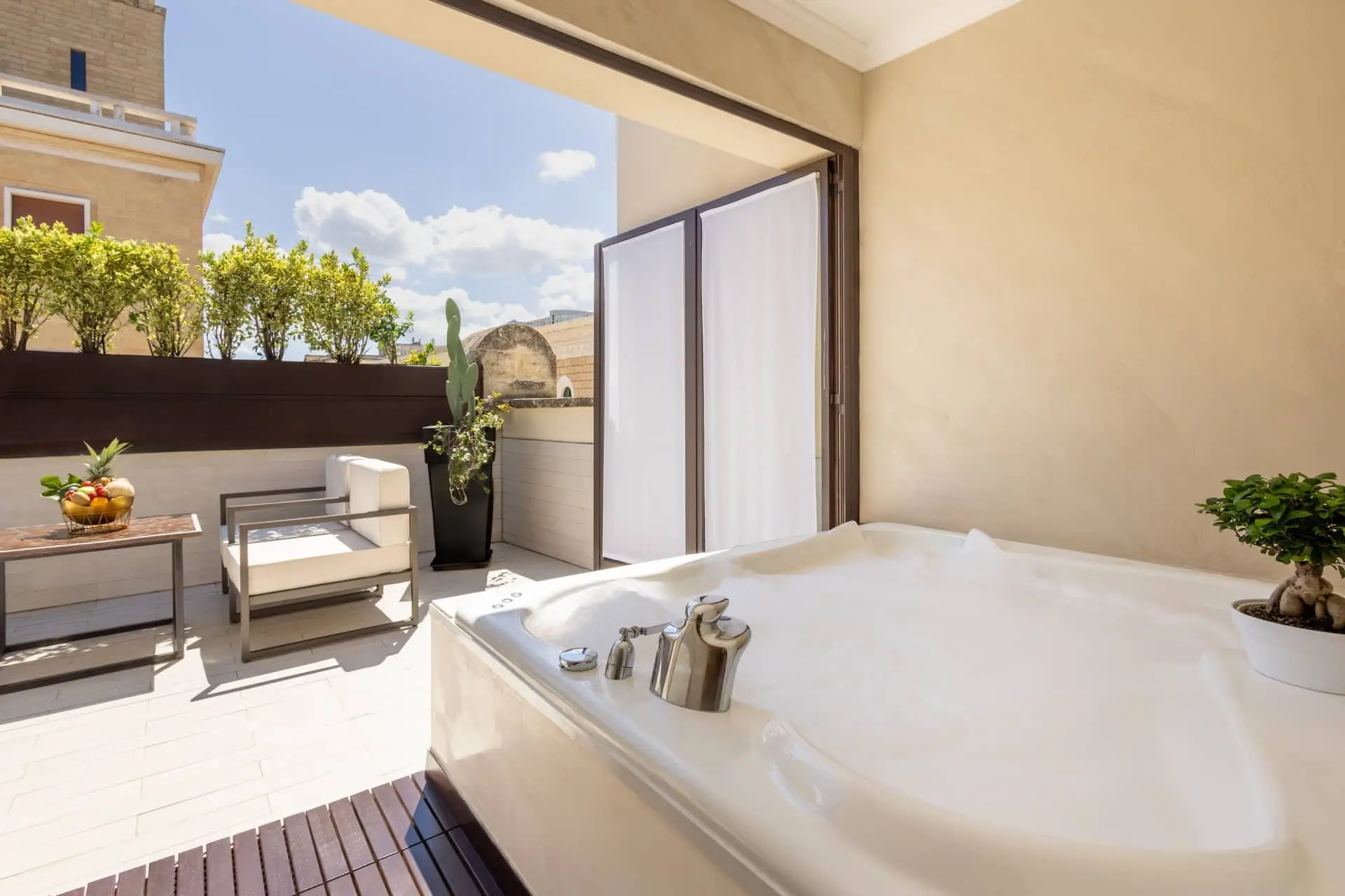 Luxury outdoor terrace with a soaking bathtub, lounge seating, and potted greenery under a sunny sky