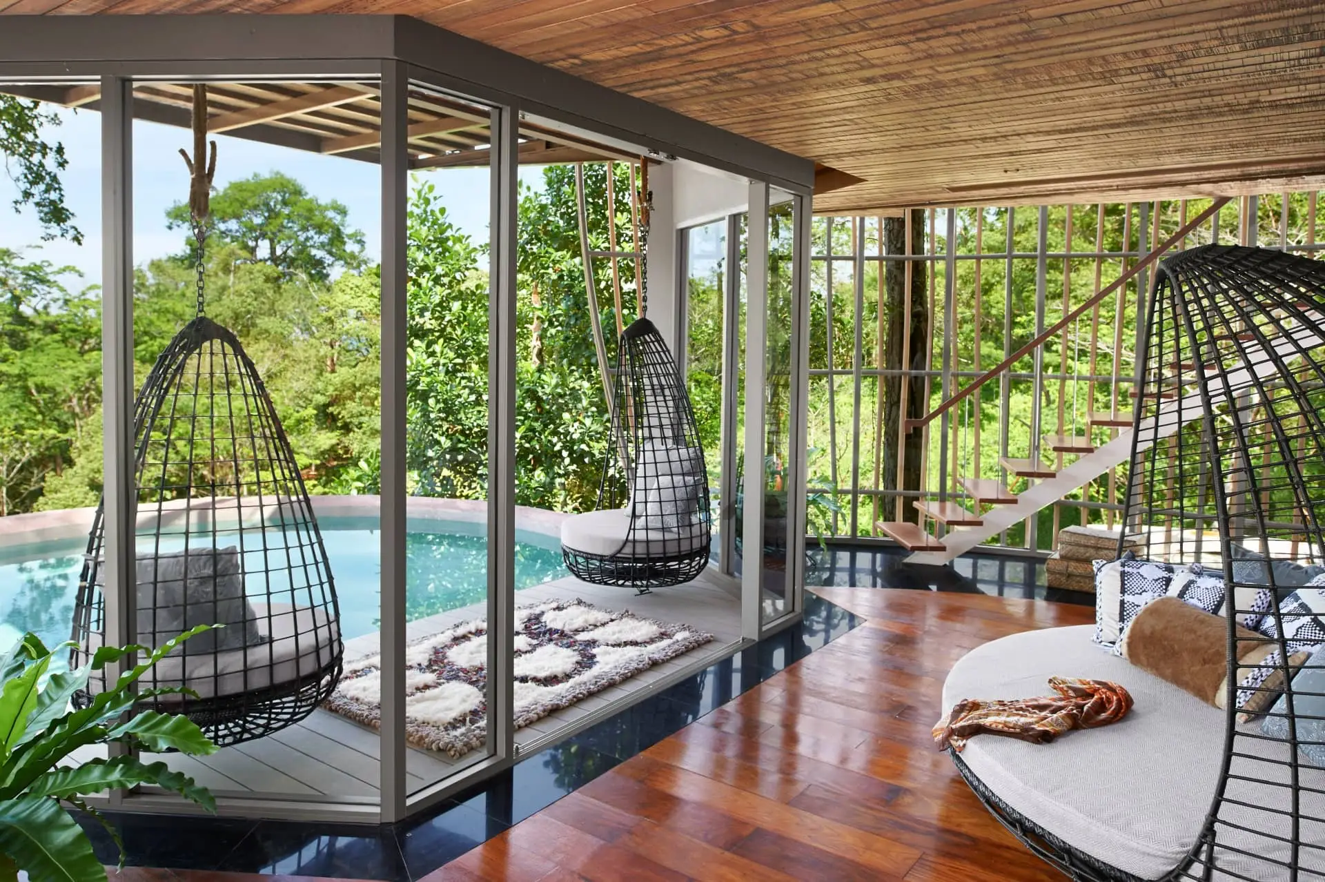 Luxury outdoor spa cabanas with hanging egg chairs beside a swimming pool