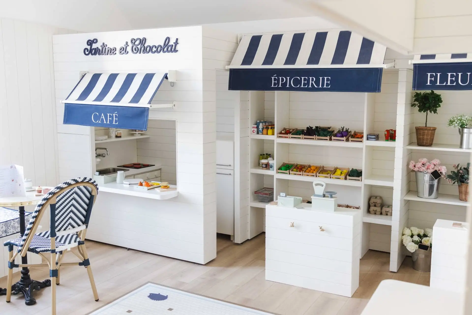 Charming white café, grocery, and flower shop display with striped awnings and outdoor seating