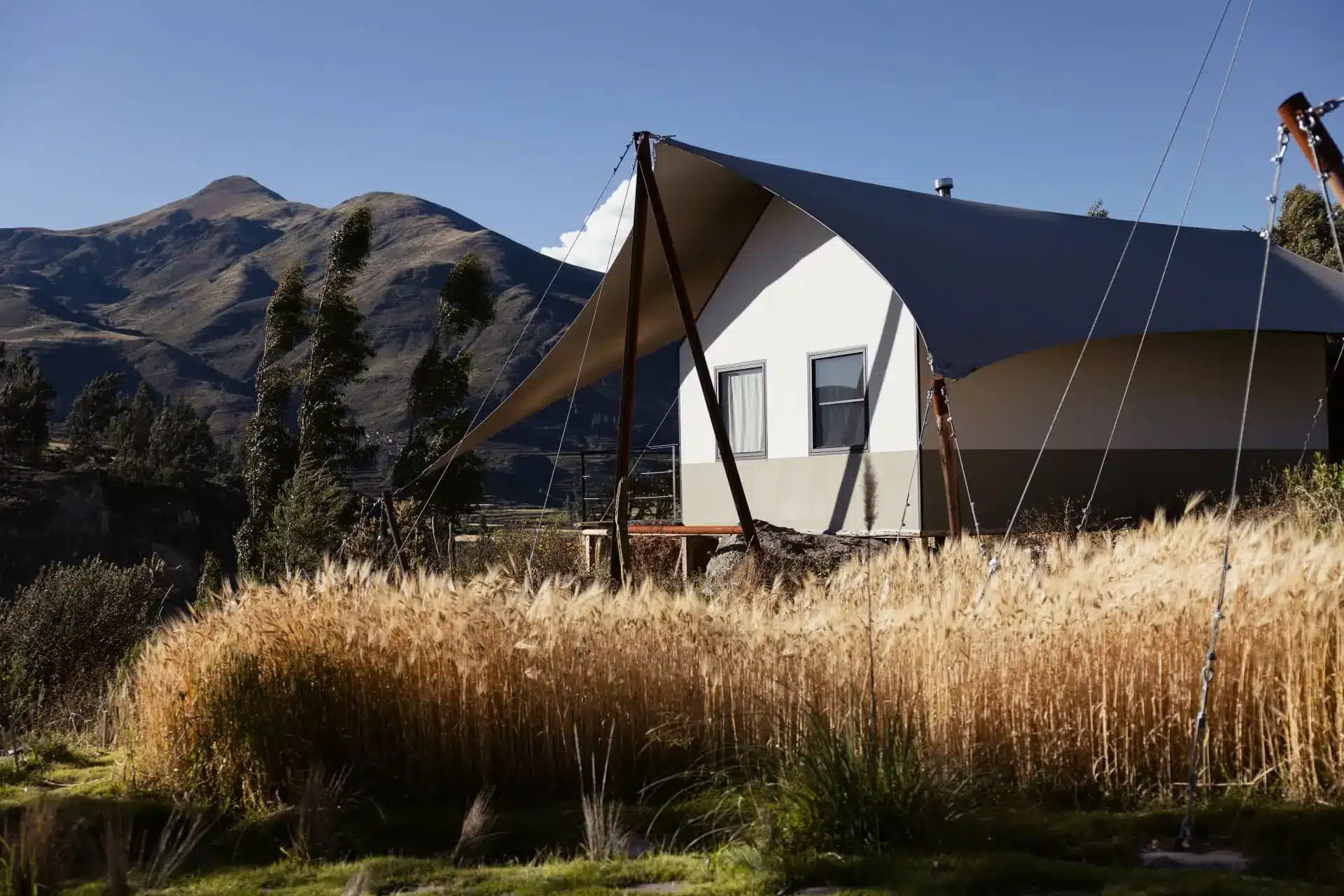 Luxury glamping tent set in golden grass beneath mountain peaks