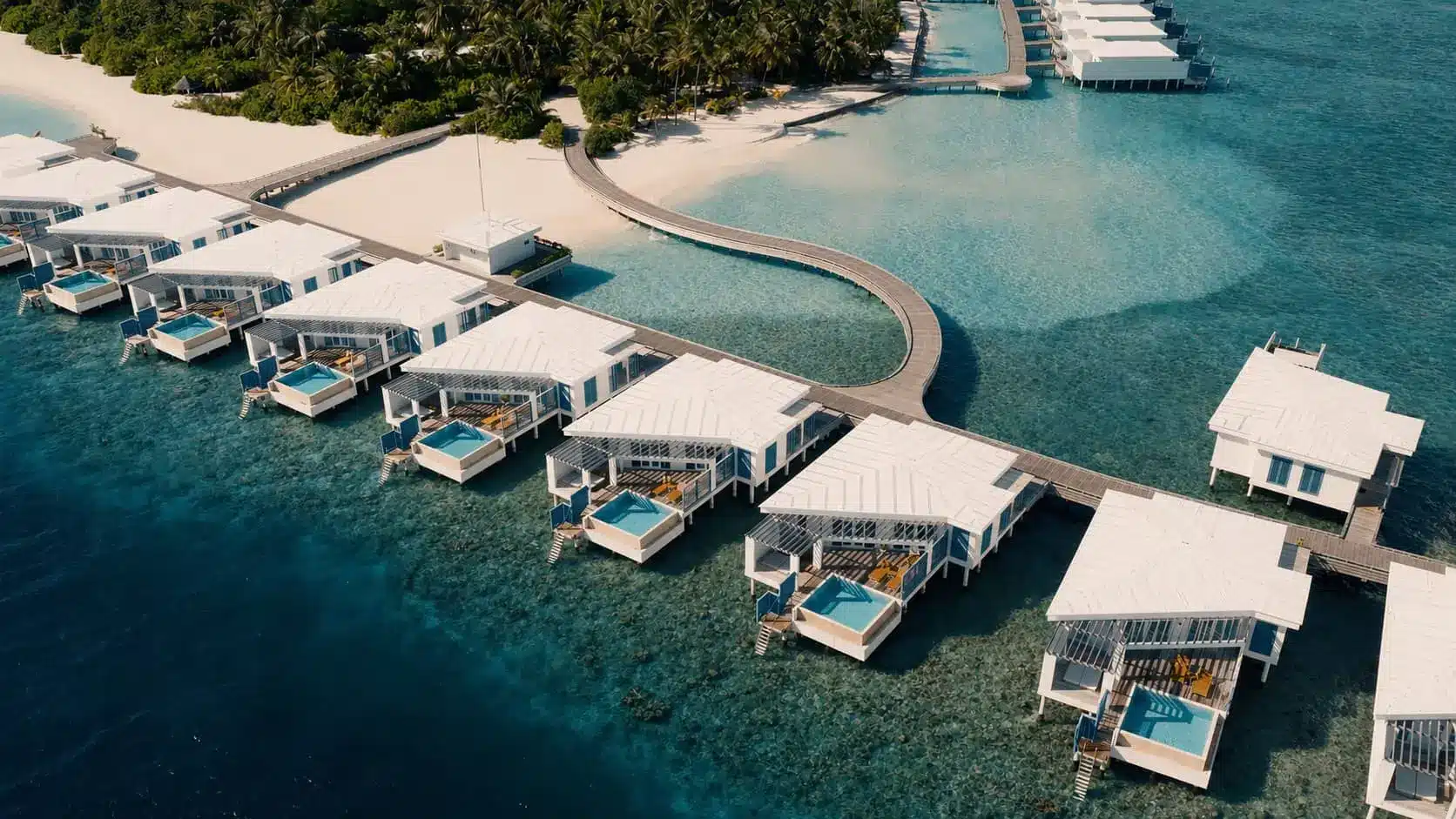 Aerial view of overwater villas and a curving infinity pool on a luxury tropical resort