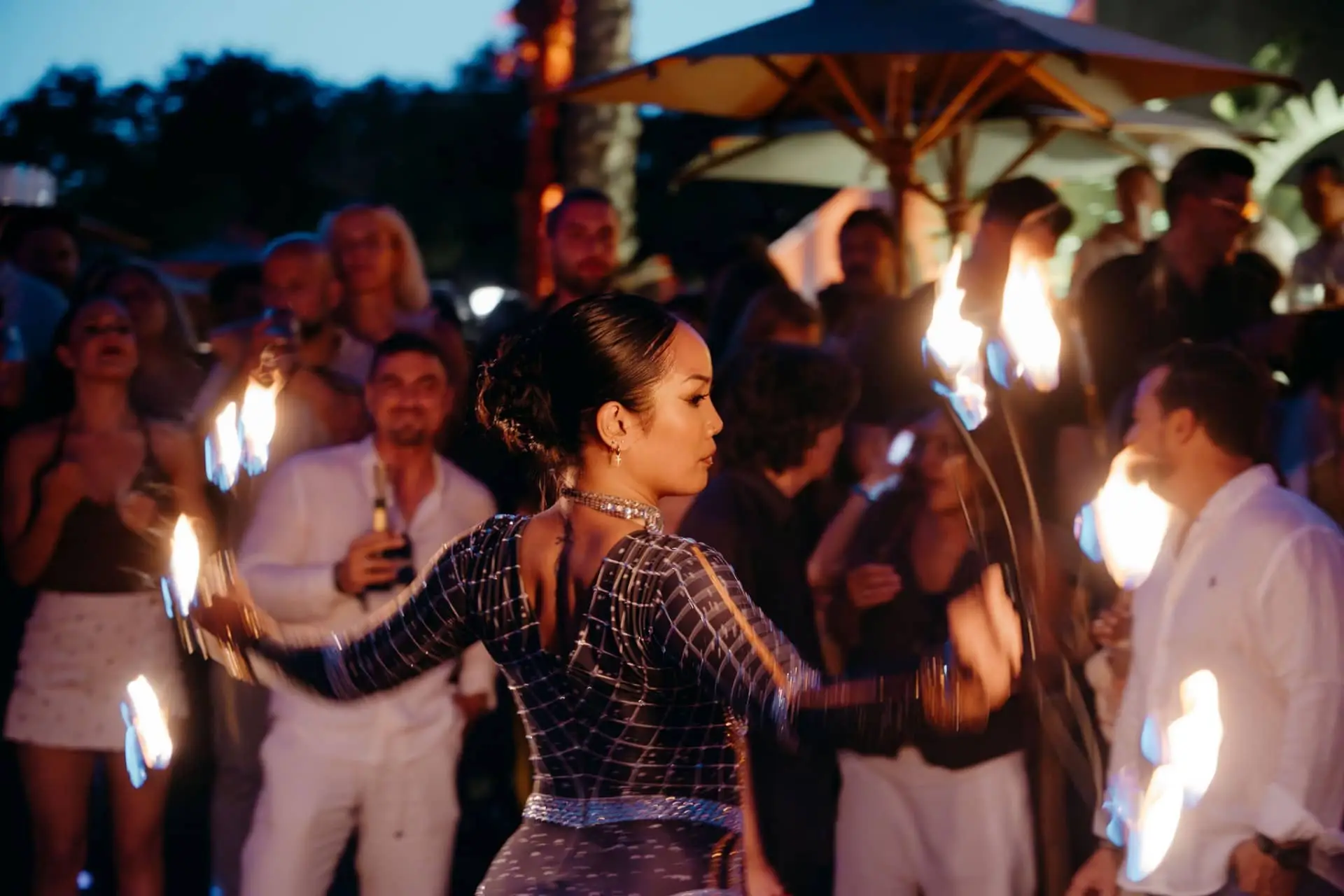Woman performs with flaming torches as guests watch at an outdoor evening party