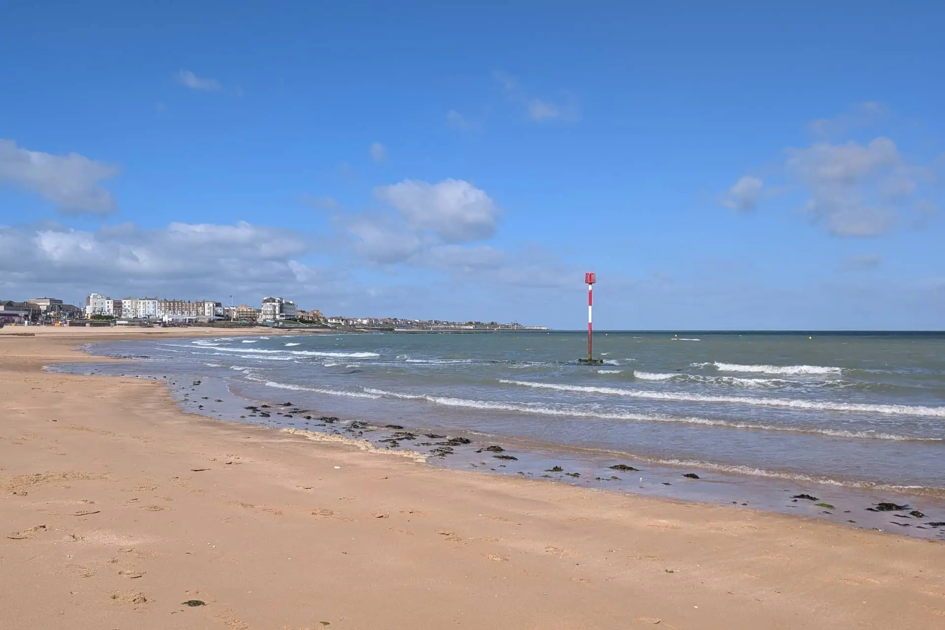 Margate Main Sands with waves, a red sea marker and seaside buildings on the horizon
