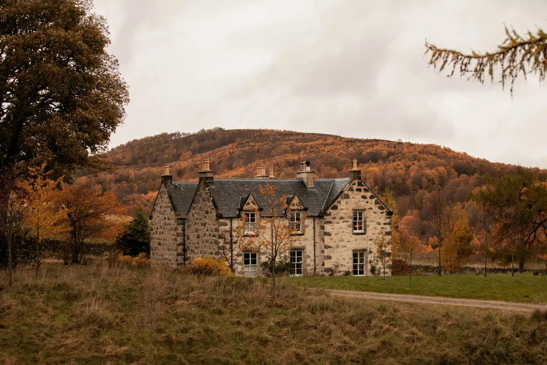 Historic stone manor house surrounded by autumn woodland and rolling hills
