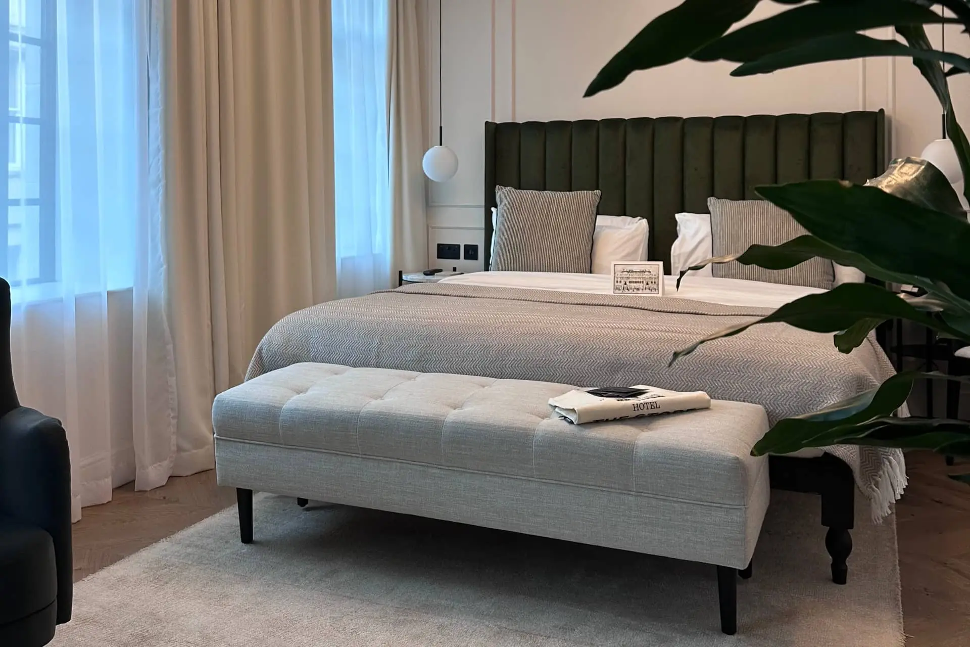 Luxury bedroom with a neatly made bed, neutral linens, and greenery by a window and curtain