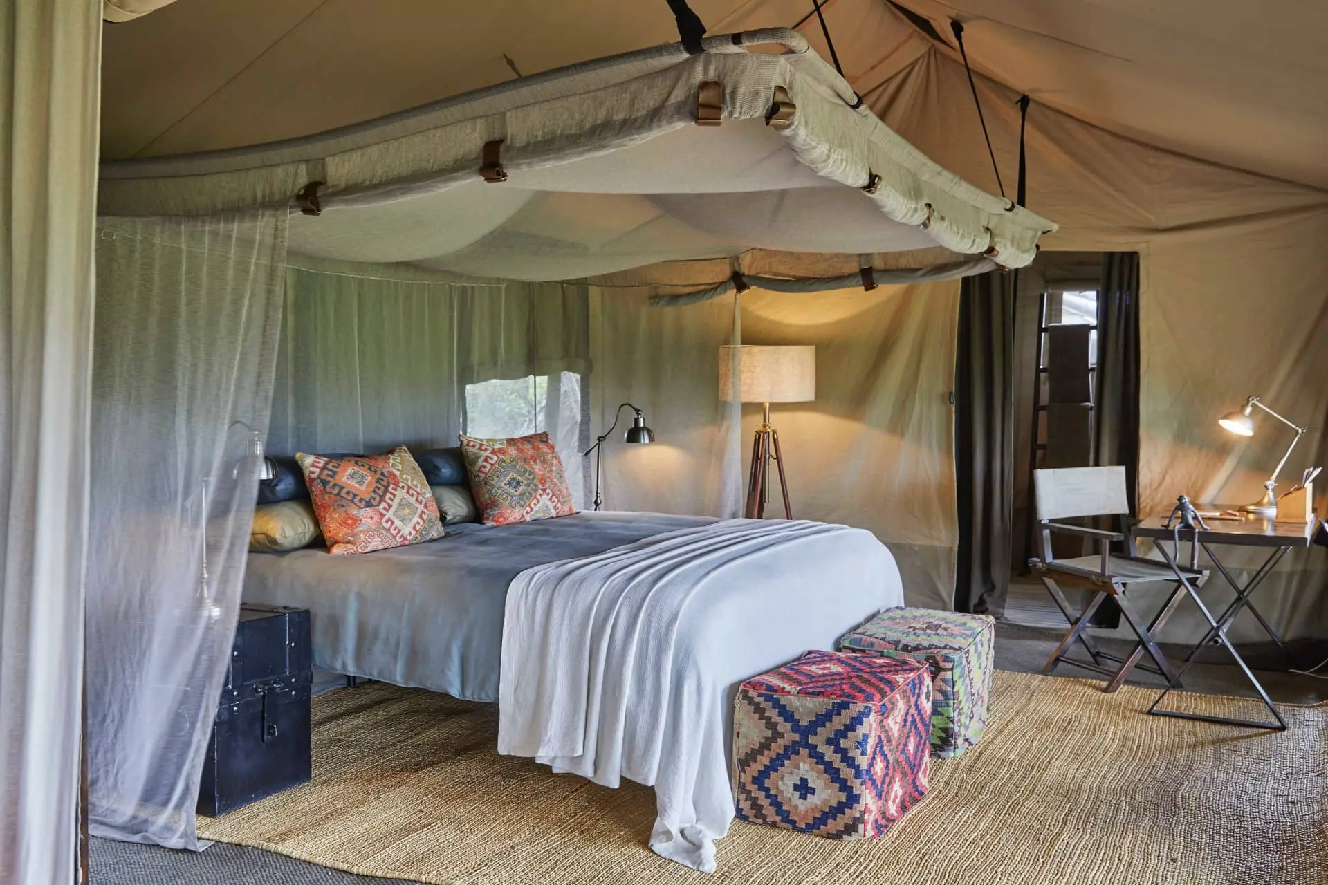 Luxury glamping tent bedroom with a canopy bed, patterned ottoman, and warm ambient lighting