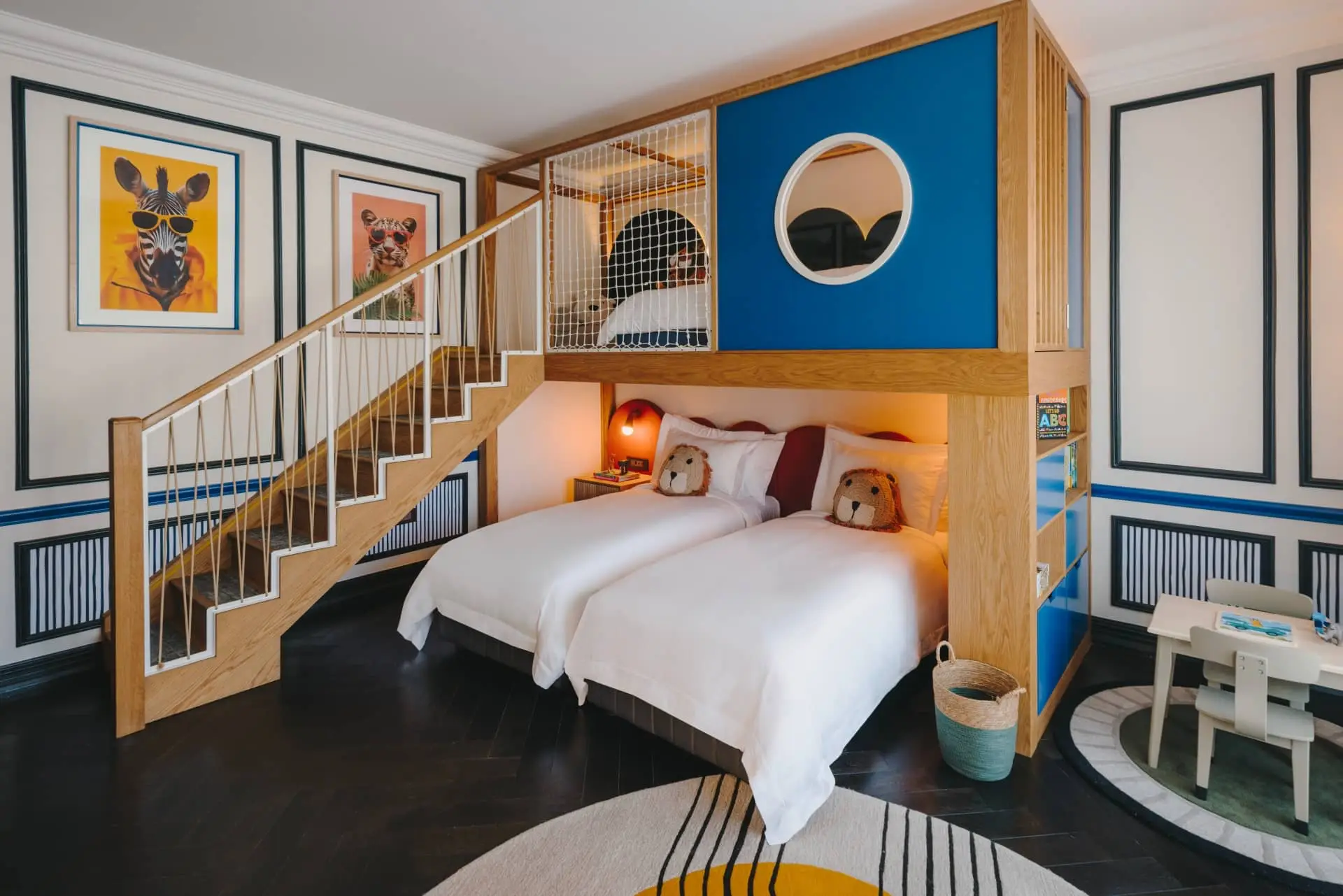 Colorful luxury hotel family suite with twin beds, a lofted play area, and staircase