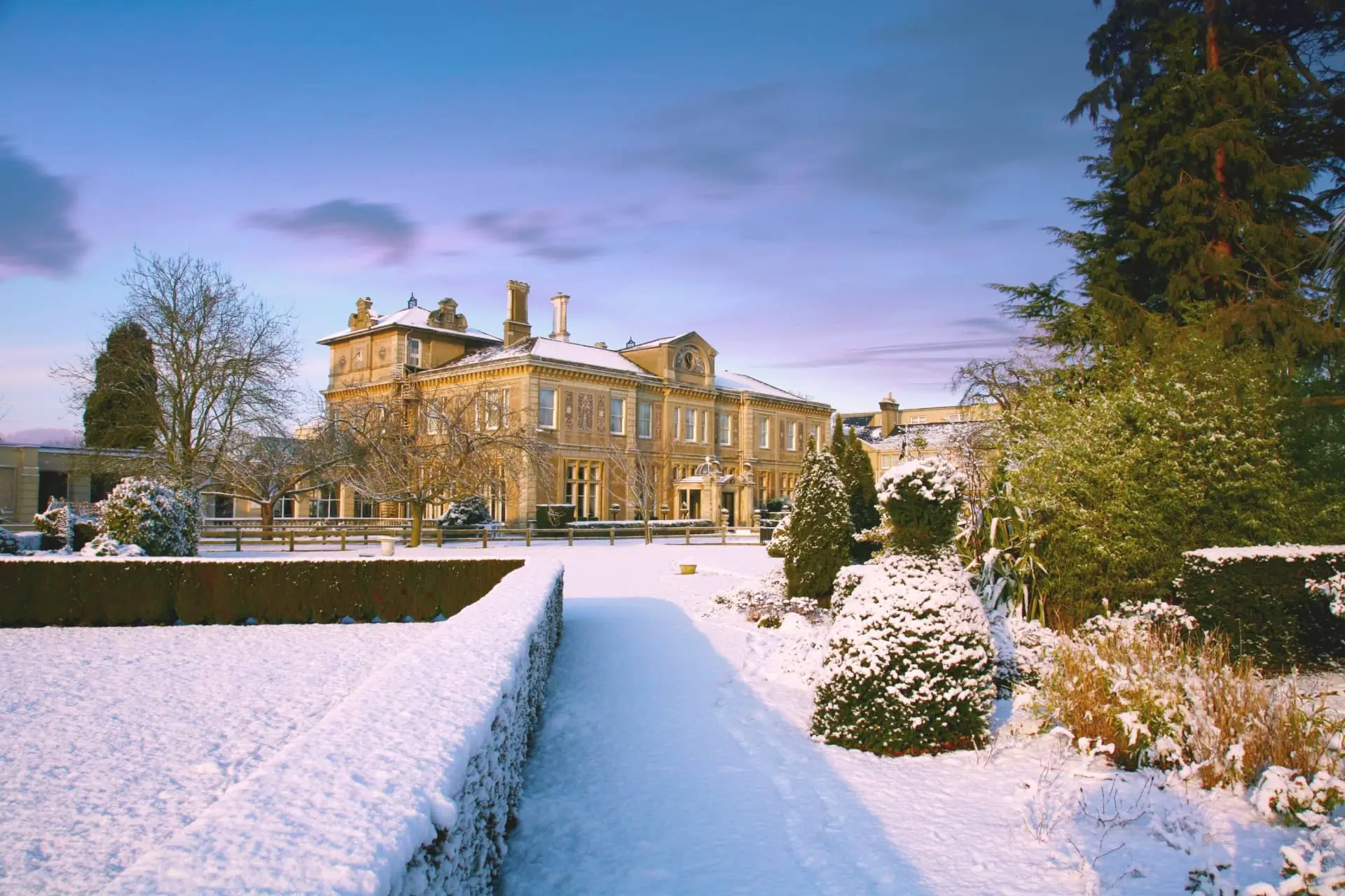 Snow-covered formal gardens leading to Down Hall Hotel, a grand country house in Essex, at dusk