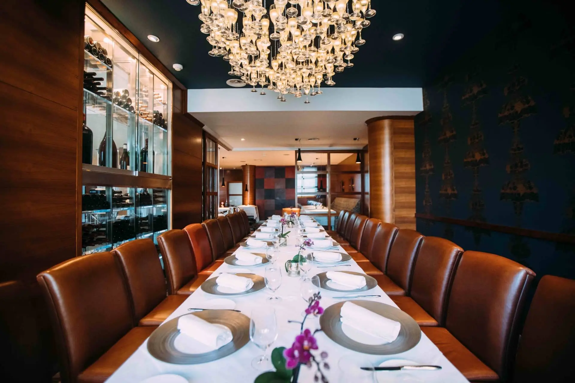 A long dining table set beneath a crystal chandelier in Bohemia restaurant at The Club Hotel & Spa, Jersey
