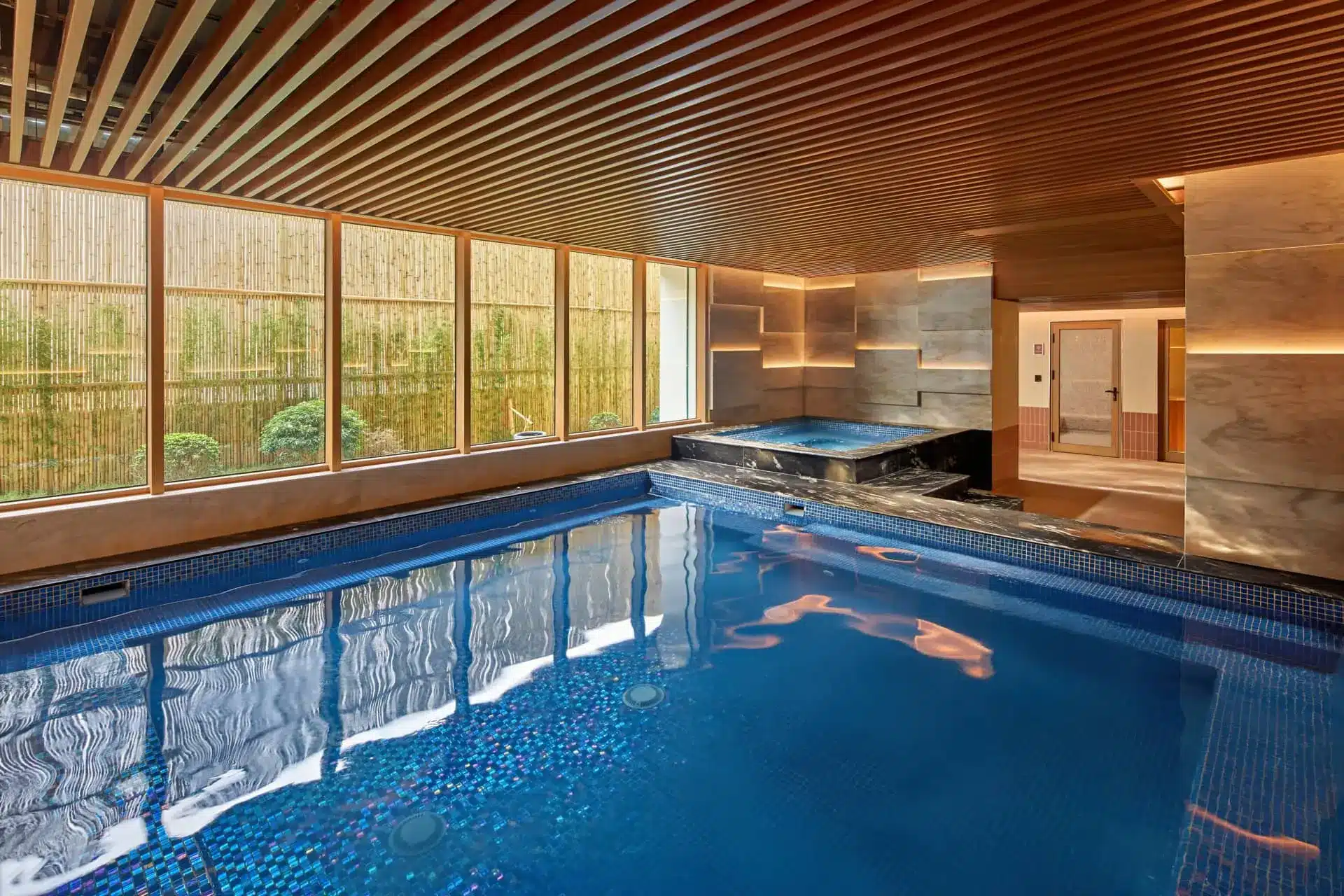 Luxury indoor swimming pool with a person relaxing beneath a slatted wood ceiling