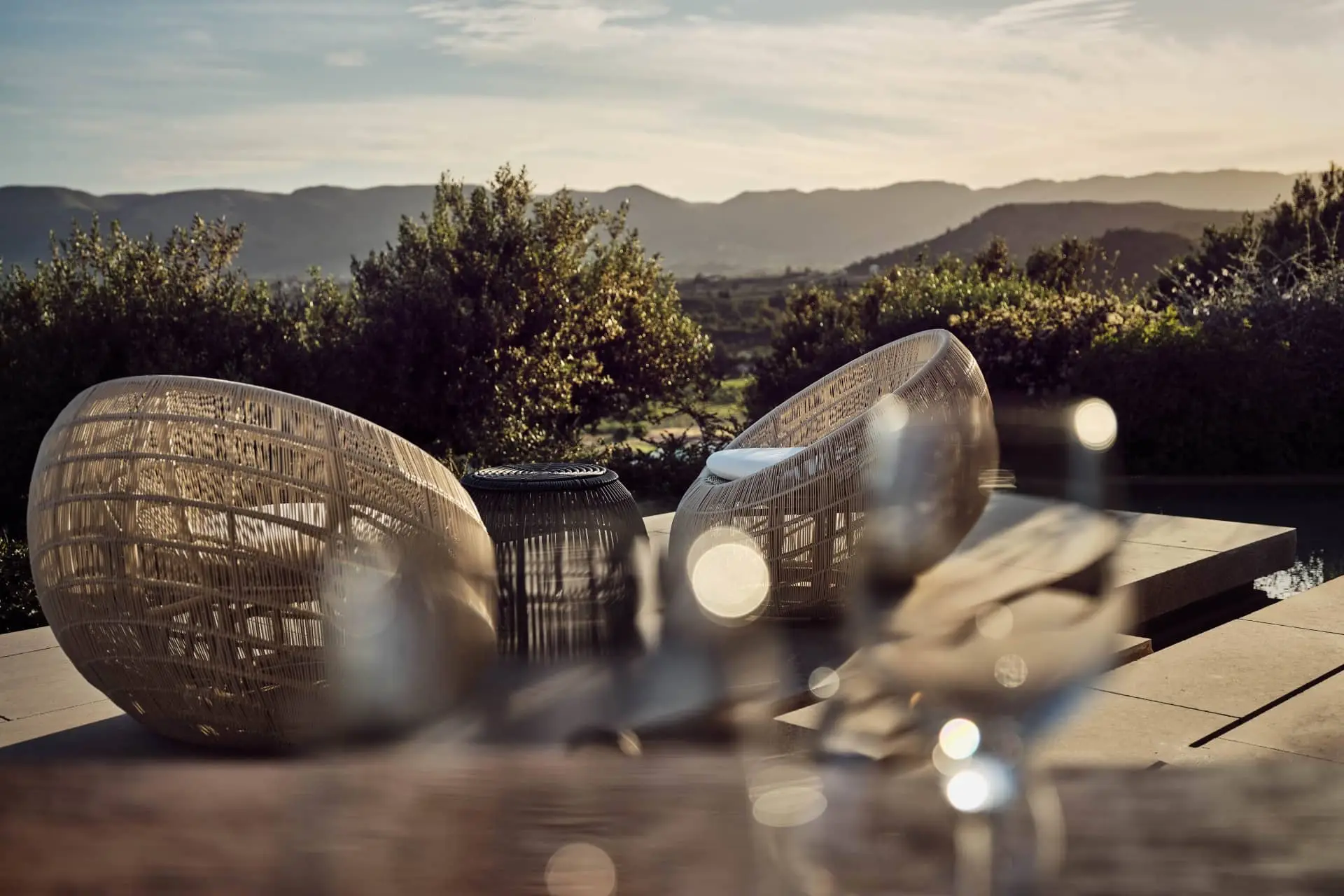 Luxury terrace with woven lounge chairs overlooking a sunlit mountain landscape