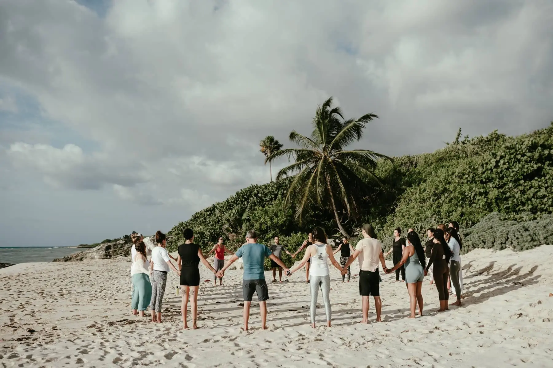 Group of travelers holding hands in a circle on a tropical beach beneath swaying palm trees