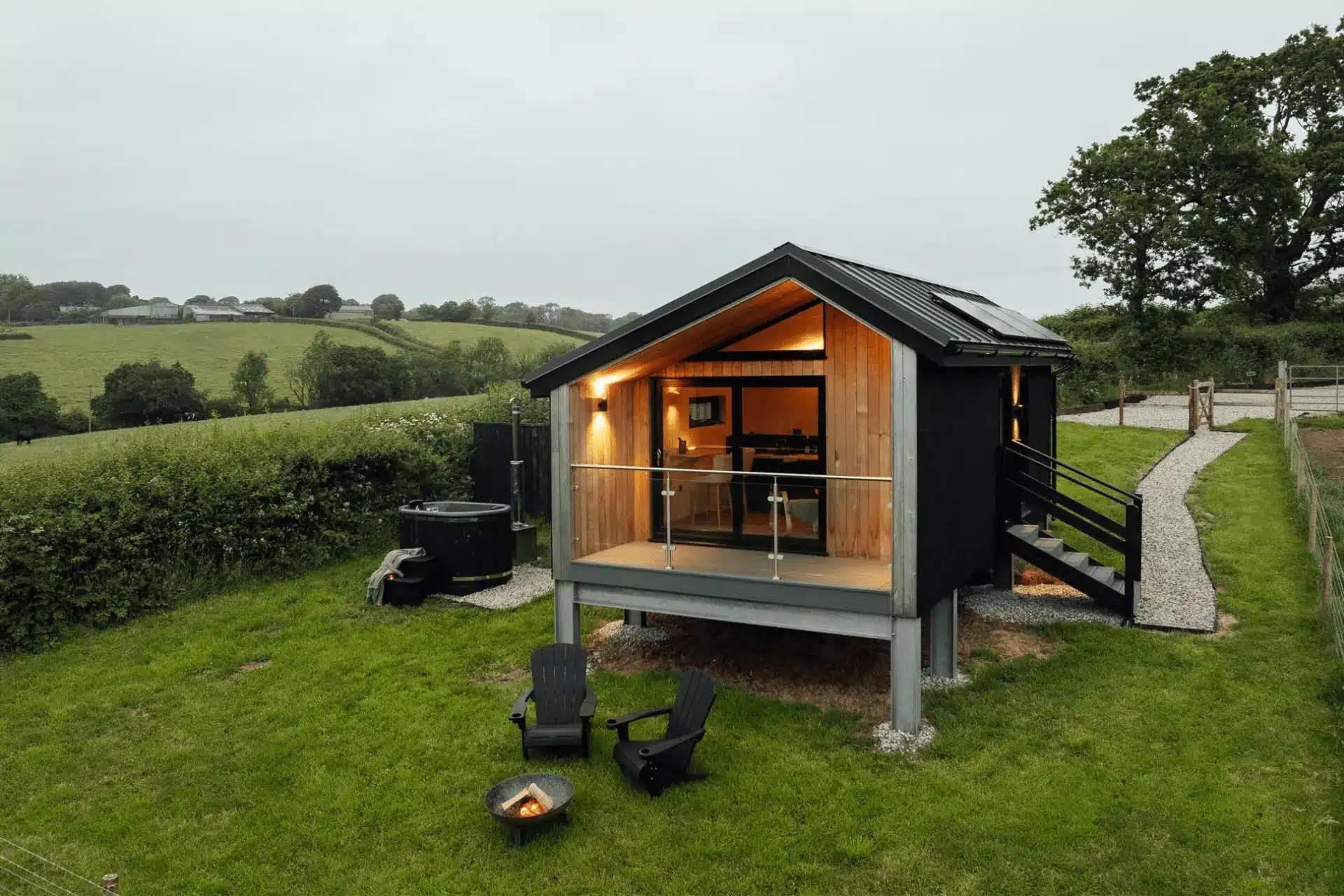 Luxury glass-fronted cabin glowing in a green rolling countryside landscape