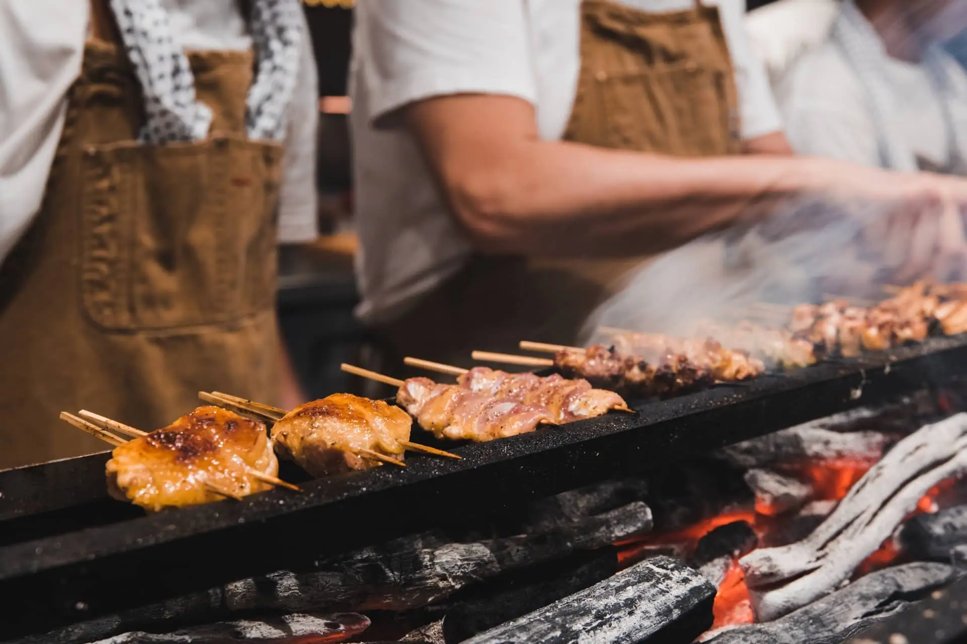 Skewers of meat grilling over glowing charcoal at an outdoor food stall