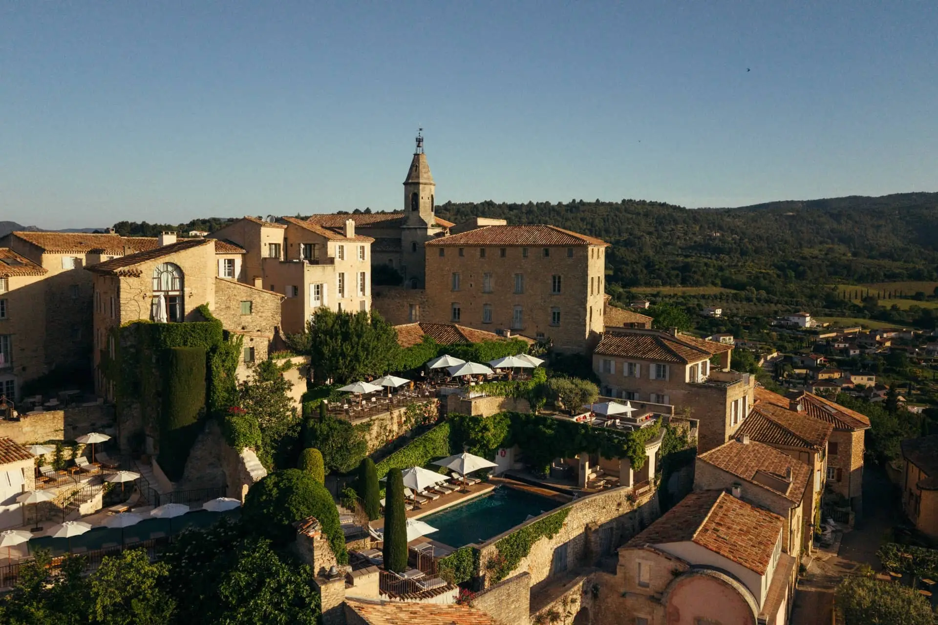 Stone houses and a church tower in Crillon le Brave overlook a pool, gardens and the Provençal hills.