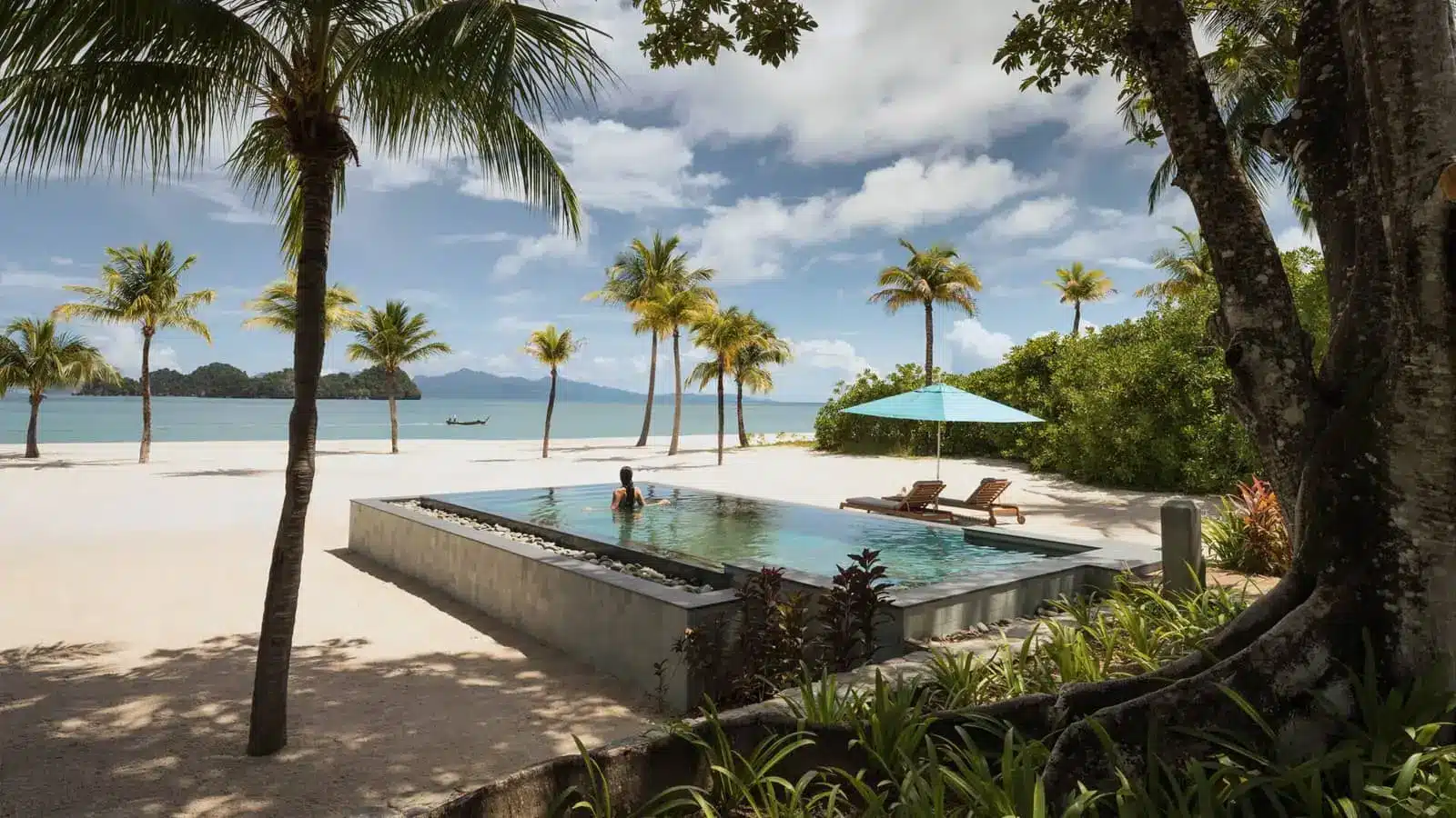 Luxury beachfront resort pool overlooking a tropical bay with palm trees and loungers