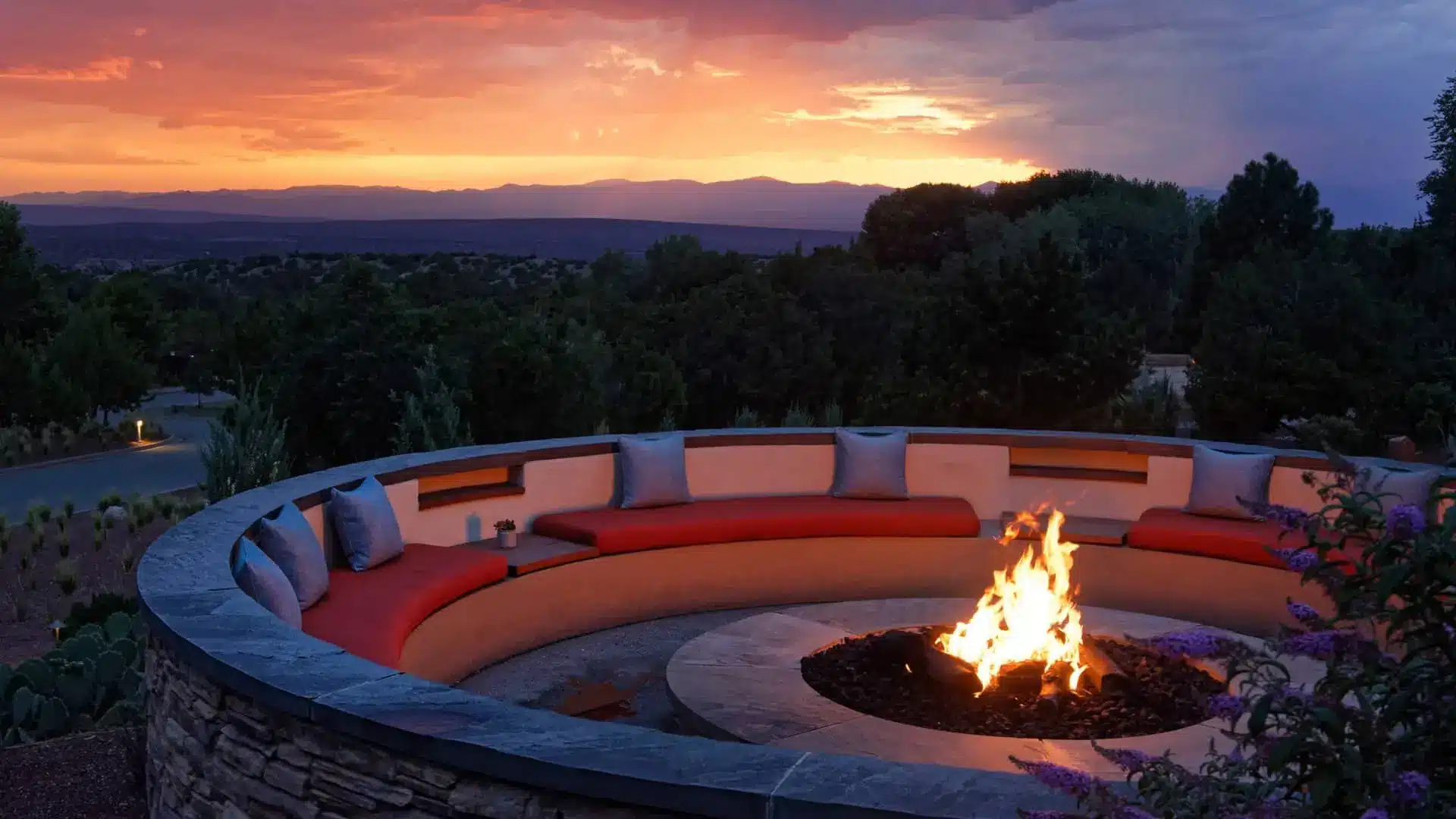 Luxury outdoor fire pit glowing at sunset beside a curved lounge overlooking distant hills
