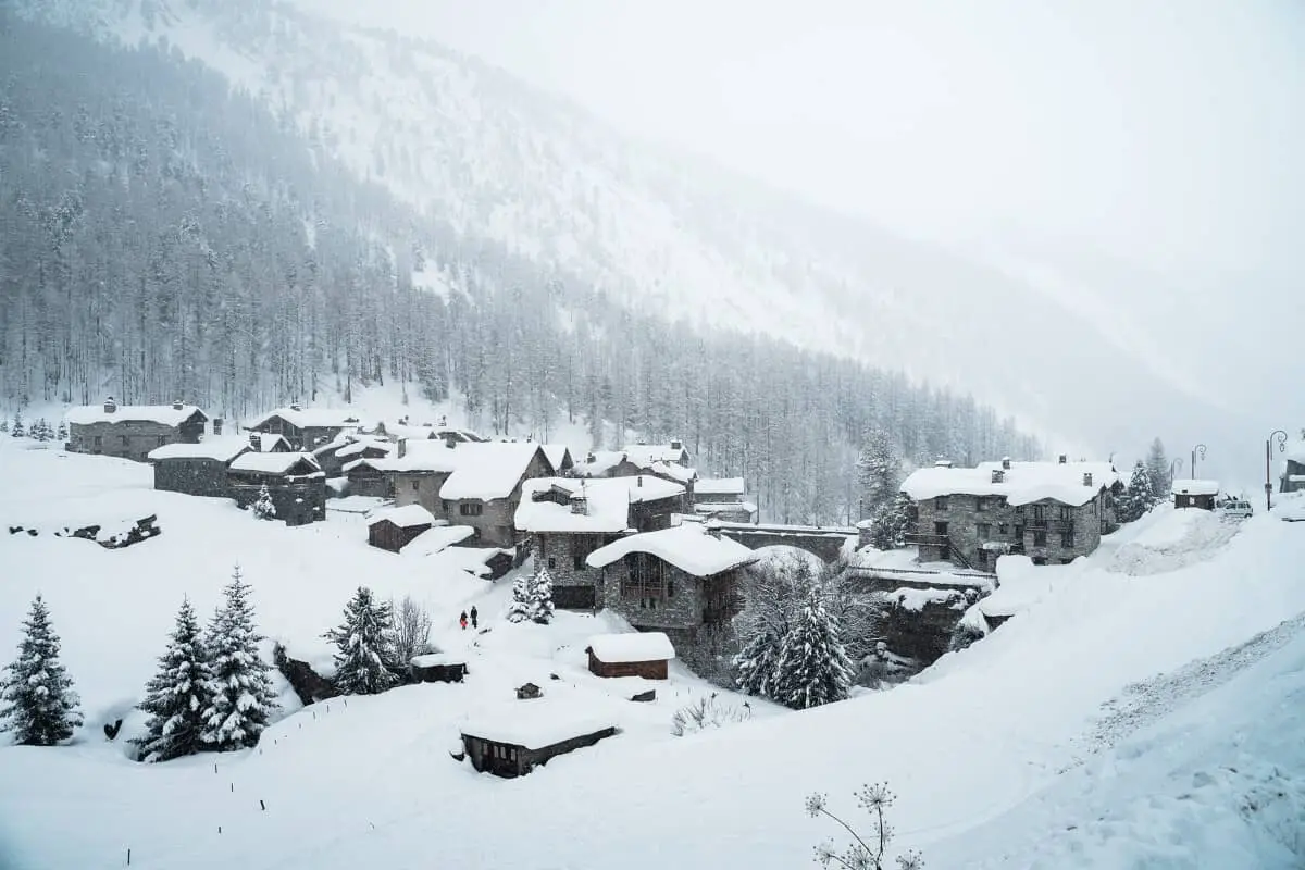 Snow-covered alpine village surrounded by pine forests and misty mountain slopes