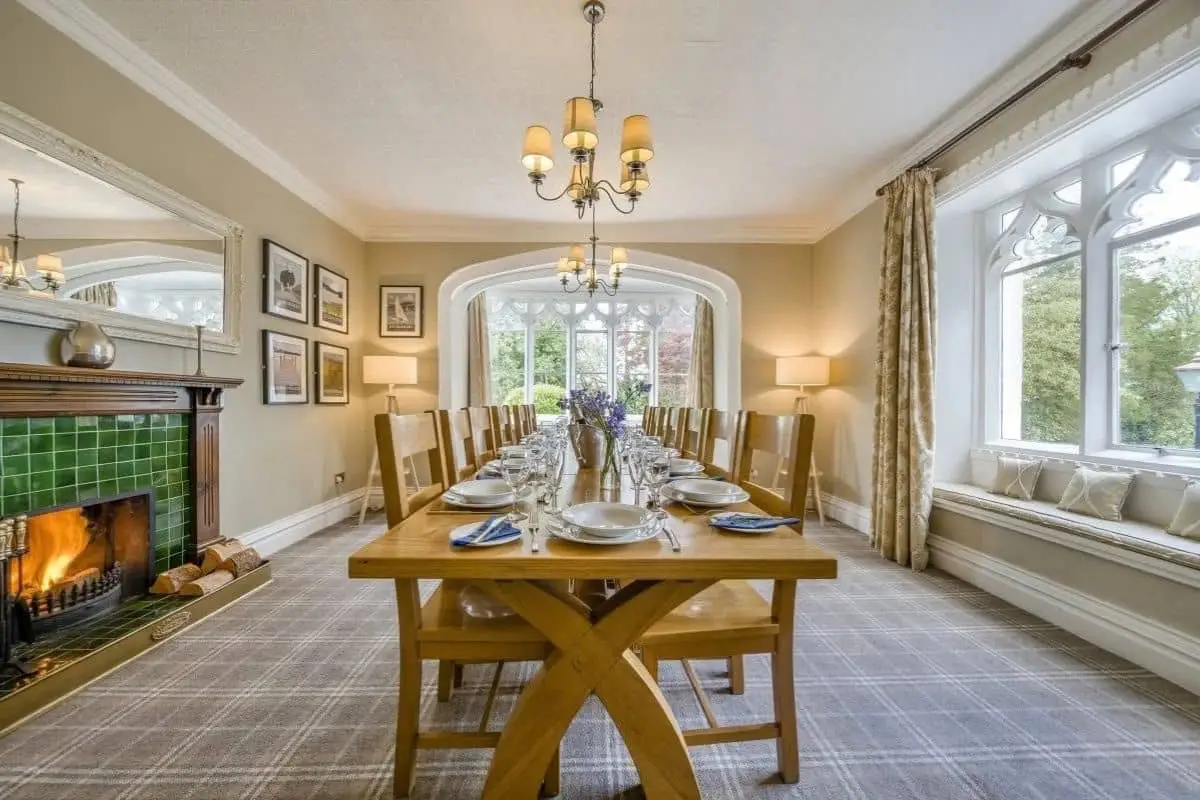 Dining room with a long table set for a group, beside a stone fireplace and large windows.