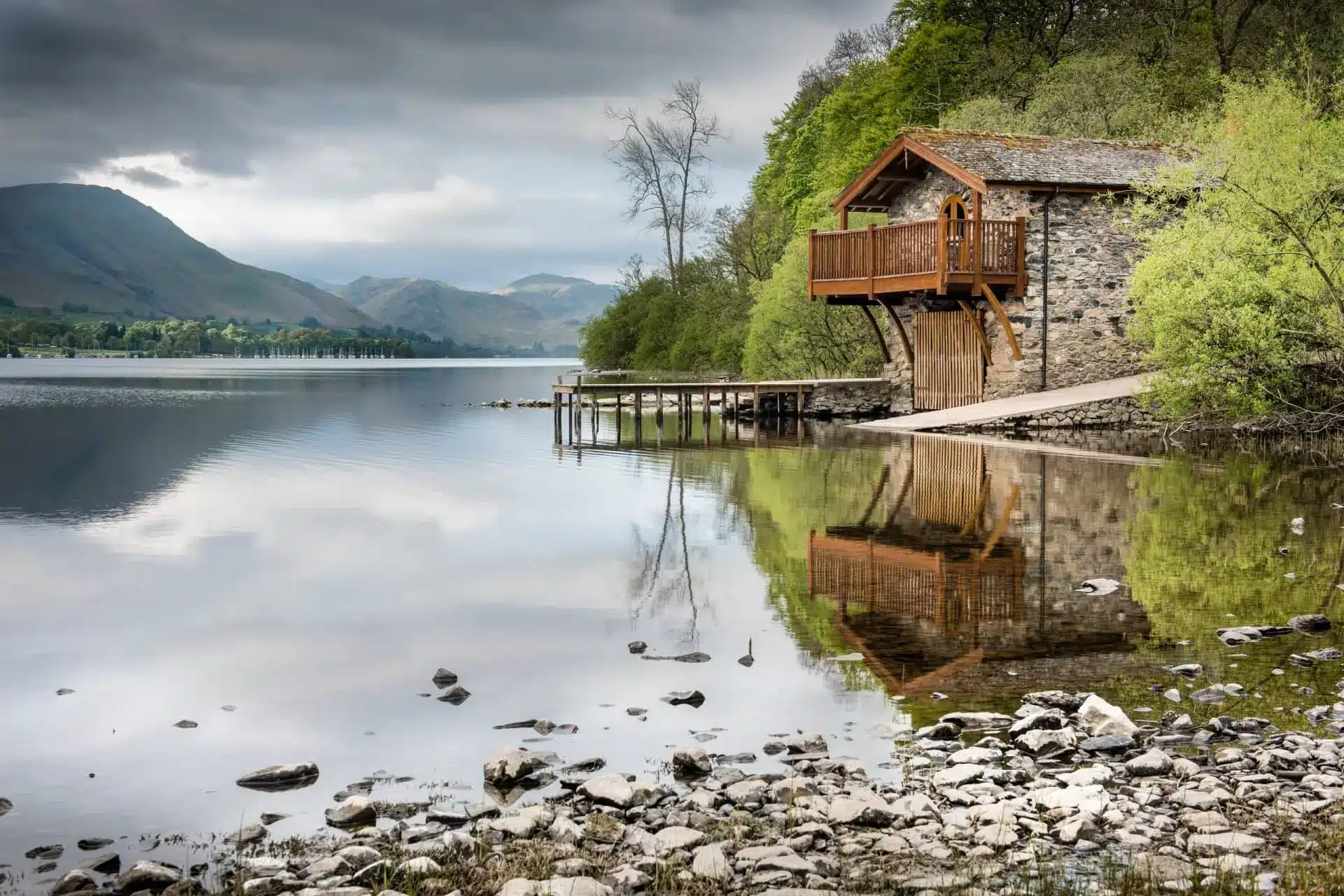 Rustic lakeside boathouse reflected in a tranquil mountain lake beneath cloudy skies