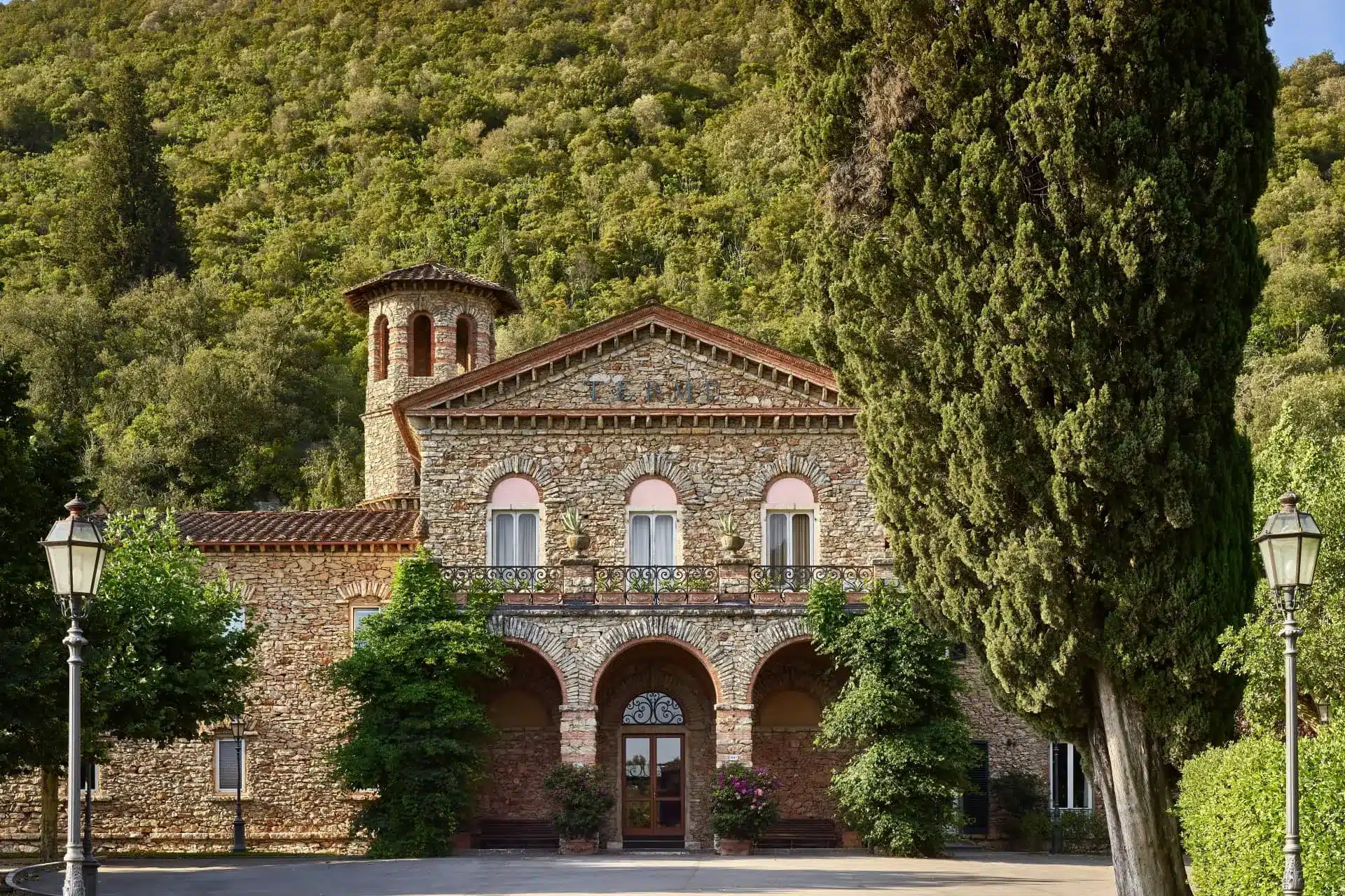 Historic stone facade of Grotta Giusti Thermal Spa Resort, framed by cypress trees and green hills