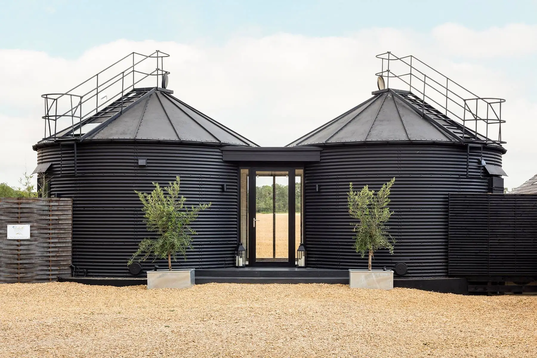 Black twin-roofed accommodation buildings with rooftop railings, potted trees, and a central glass entrance