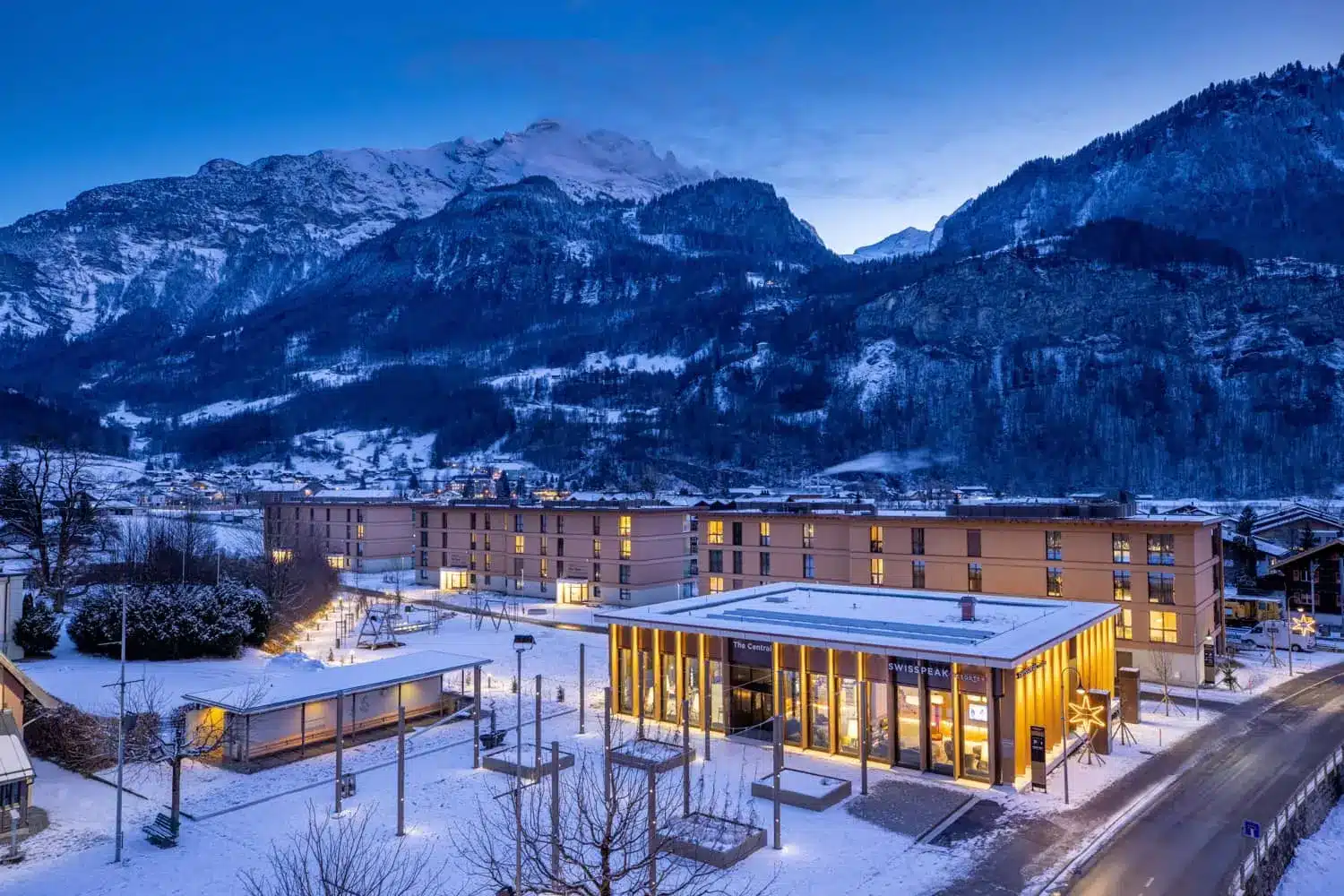 Snow-covered Alpine resort with a modern hotel complex beneath rugged mountains at dusk