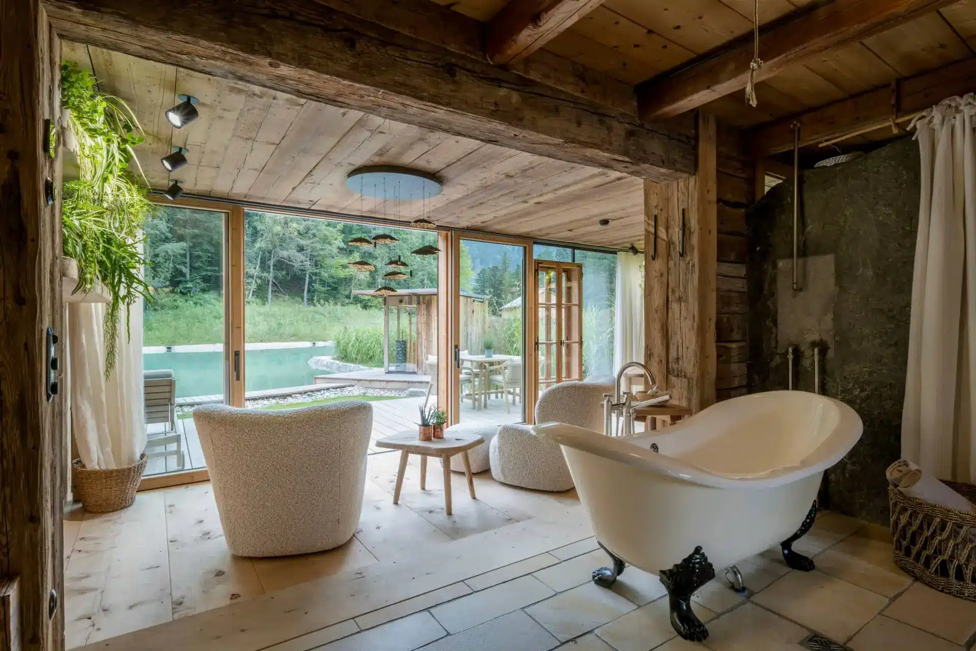 Rustic luxury bathroom with a freestanding tub overlooking a forest and swimming pool