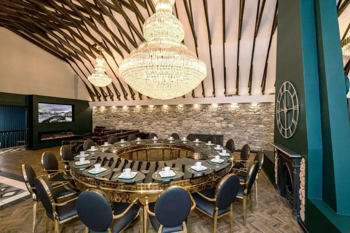 Elegant luxury restaurant dining room with a round table, blue chairs, chandeliers, and stone walls