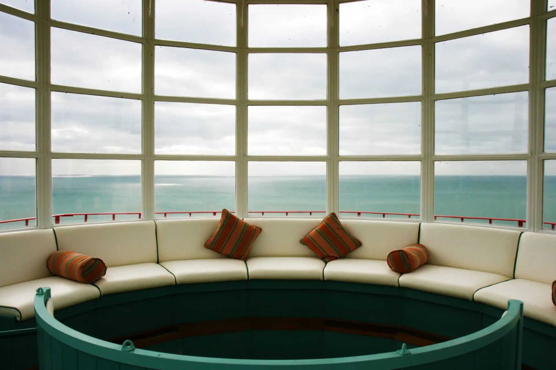 Curved luxury lounge with cushioned seating overlooking a turquoise sea through tall windows