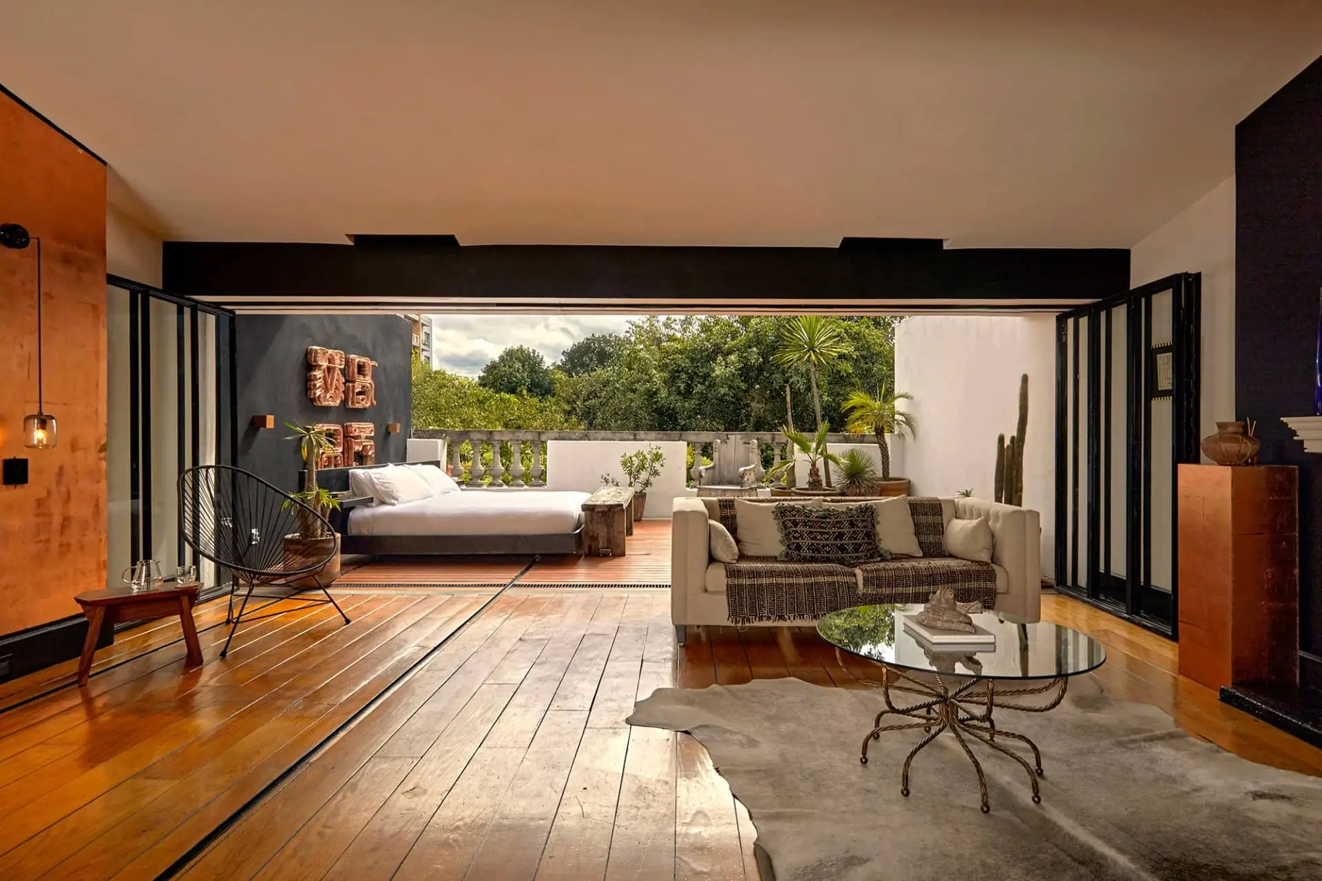 Luxury villa living room opening onto a sunlit terrace with sofas, tropical greenery, and polished wood floors