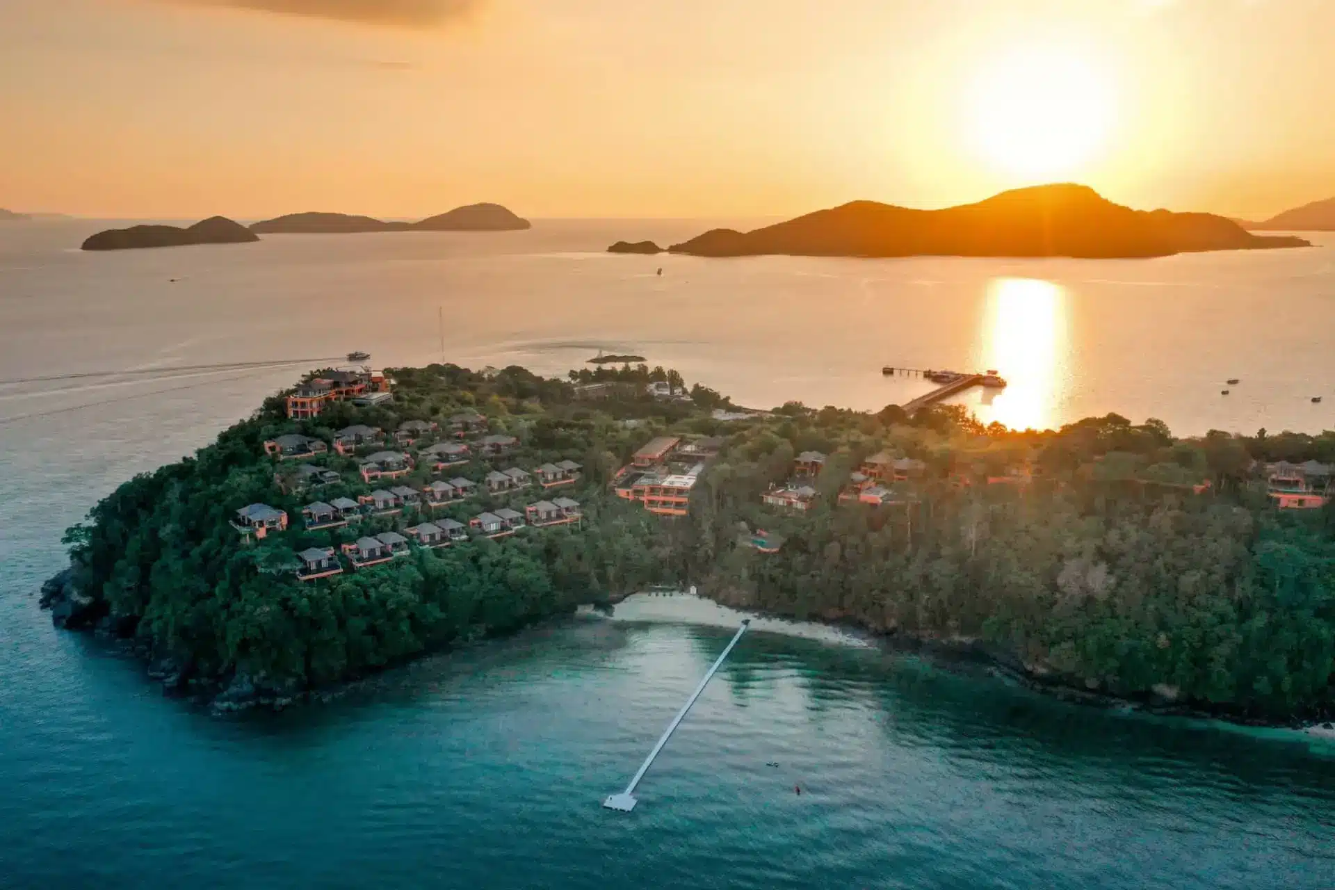 Aerial view of a forested Cape Panwa headland and resort villas at sunset, with the Andaman Sea beyond.