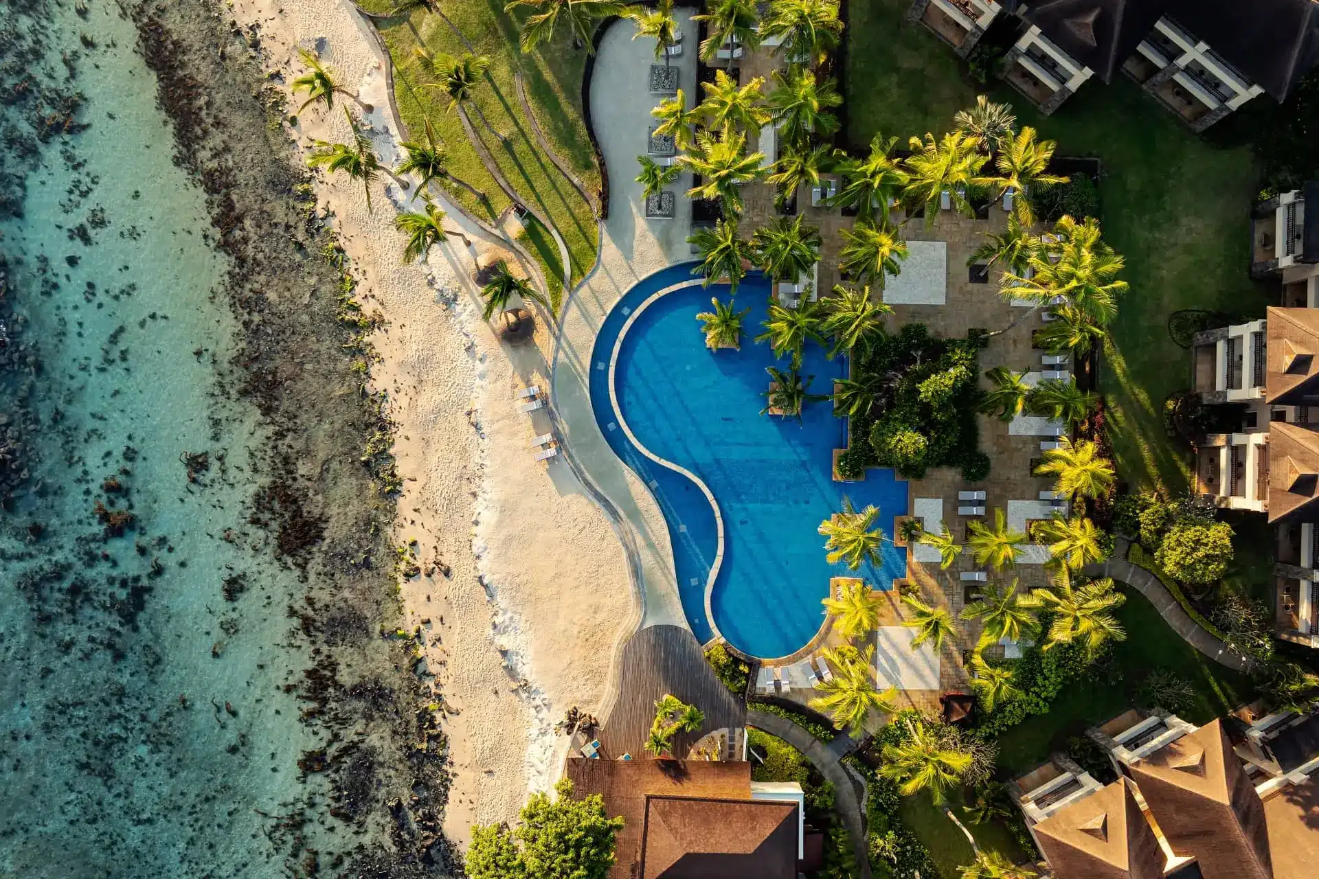 Aerial view of The Westin Turtle Bay Resort, with a curving pool, palm trees and beach beside turquoise water.