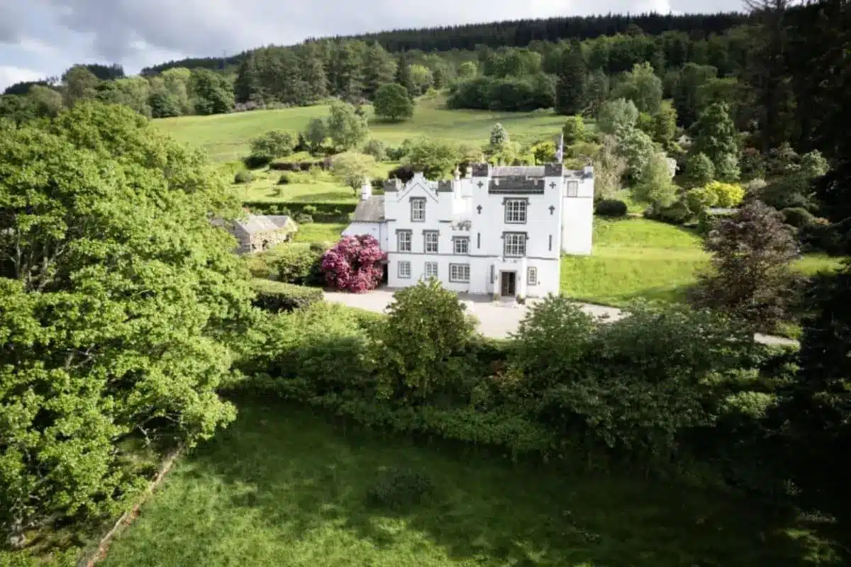 White manor house surrounded by lush gardens, rolling meadows, and woodland