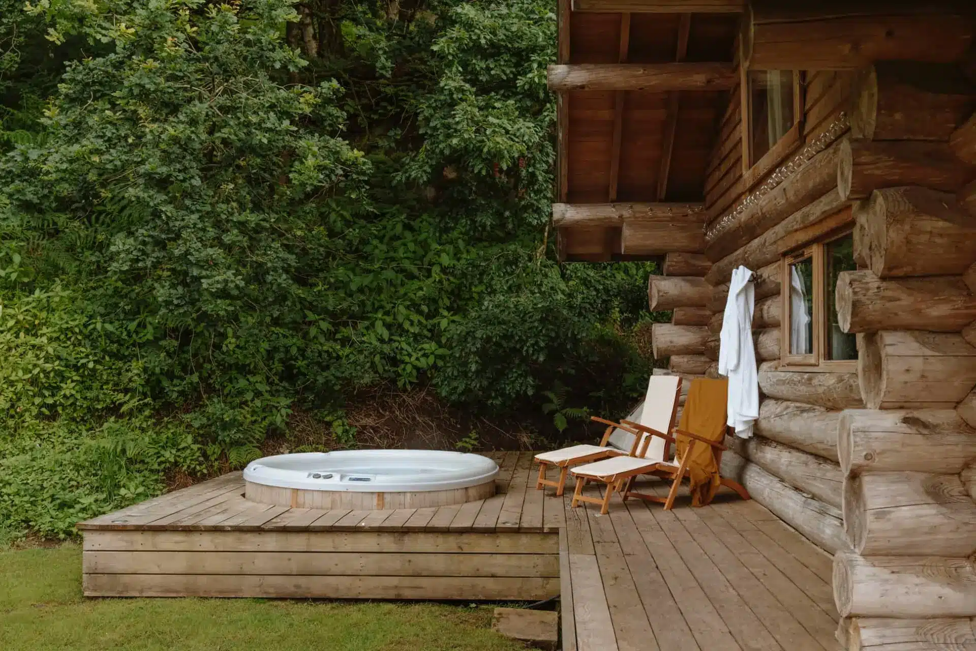 Luxury log cabin with a hot tub and chairs on a forest-surrounded wooden deck