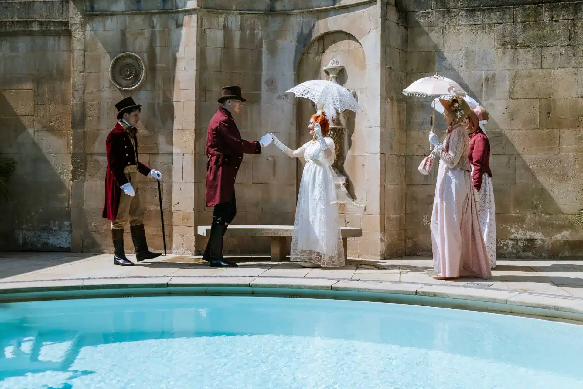 Two costumed Regency-era figures greet each other beside the thermal pool at The Gainsborough Bath Spa.