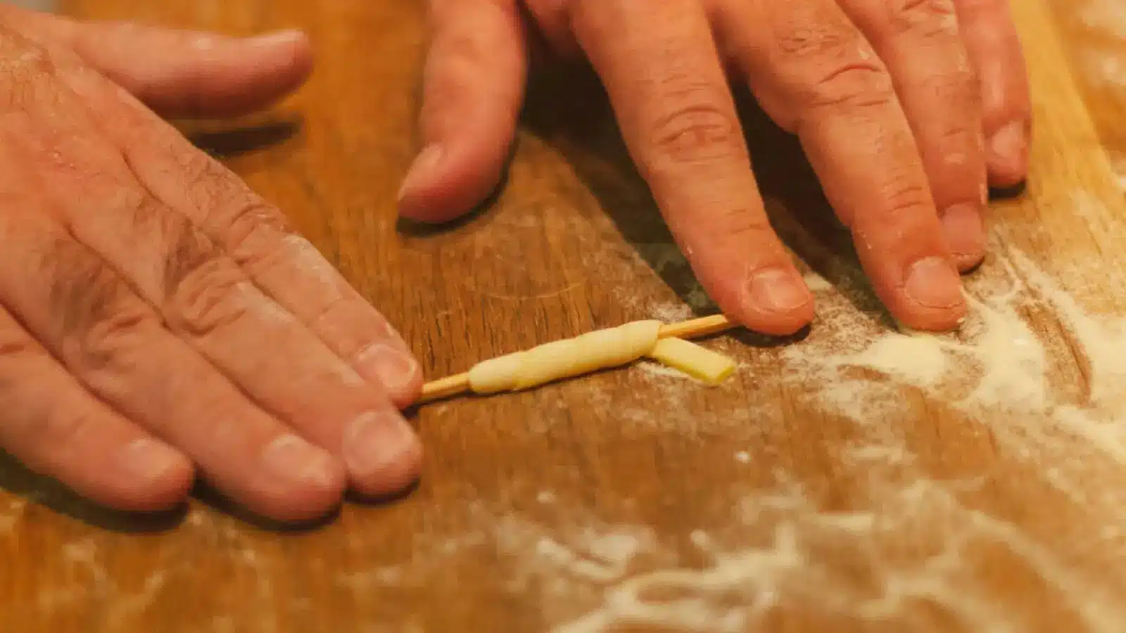 Hands shape a small piece of pizza dough on a floured wooden work surface.