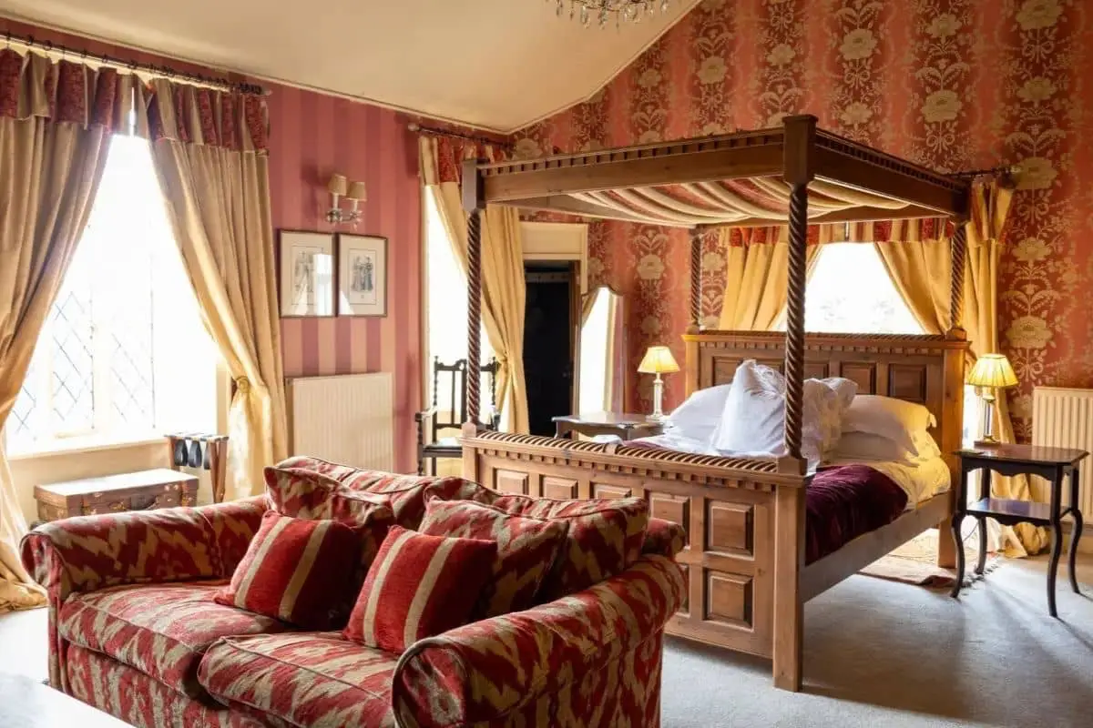 A four-poster bed and red patterned sofas in a richly decorated bedroom.