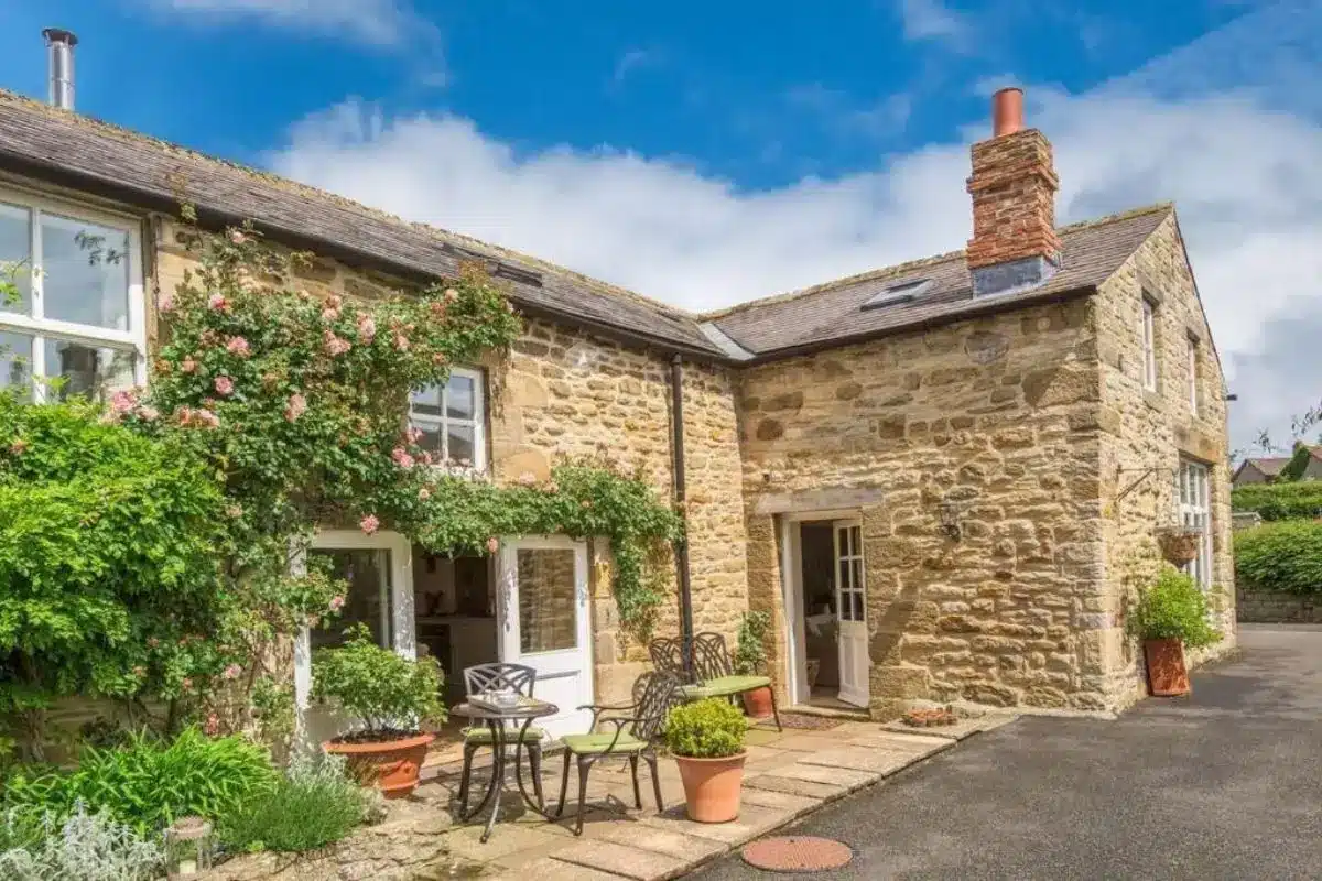 Stone cottage with a flower-covered facade and a quiet paved patio with outdoor seating