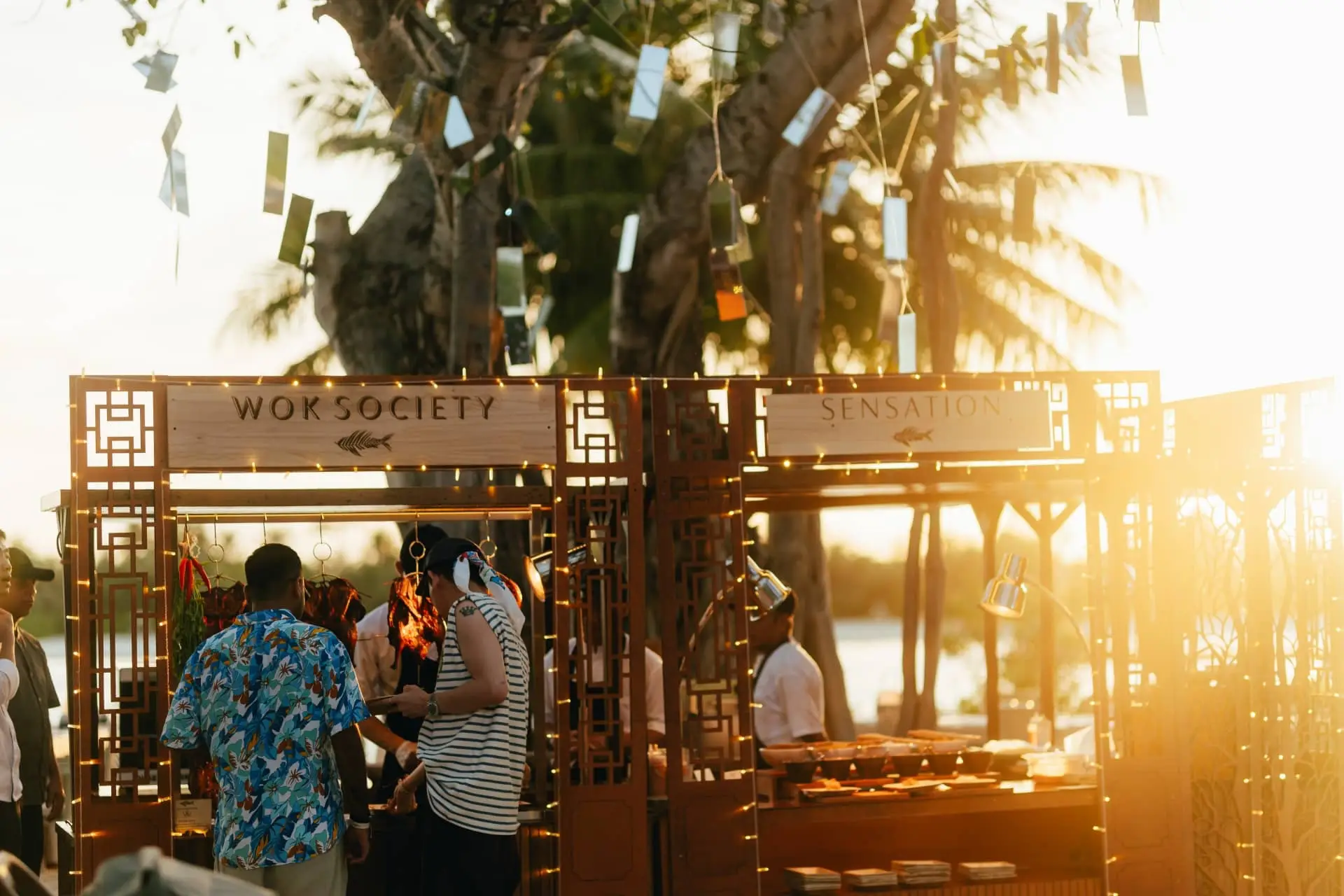 Two festivalgoers stand at a restaurant counter, one wearing a blue patterned shirt and the other a striped top.