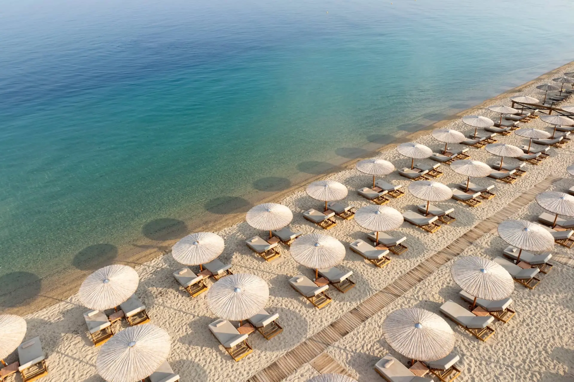 Aerial view of a luxurious beach lined with umbrellas and sun loungers beside clear turquoise water