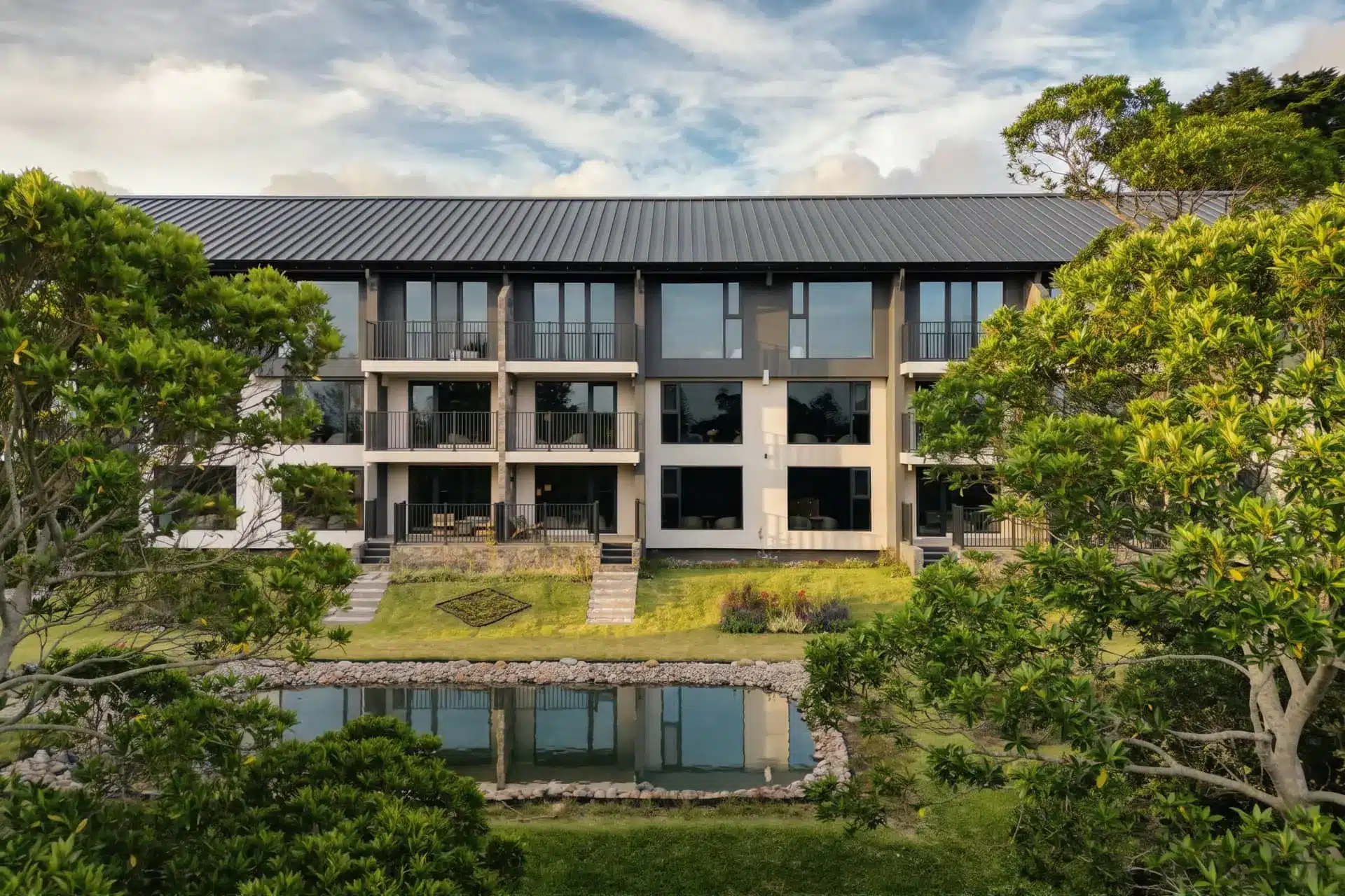 Montara Hotel’s modern multi-story building, framed by trees and gardens, with a low poolside structure in front.