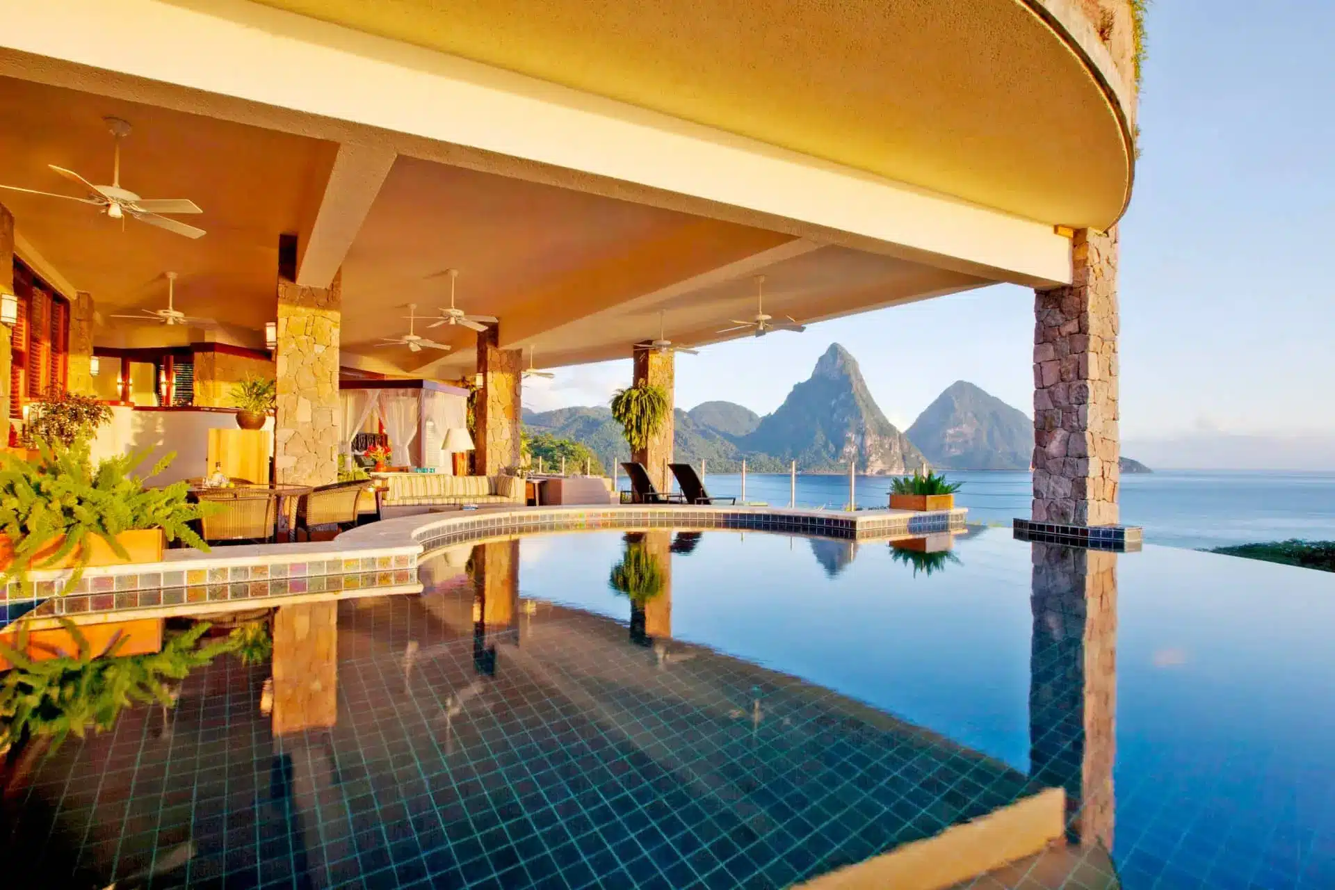 Jade Mountain’s infinity pool overlooks Saint Lucia’s Pitons beside an open-air lounge and palm trees.