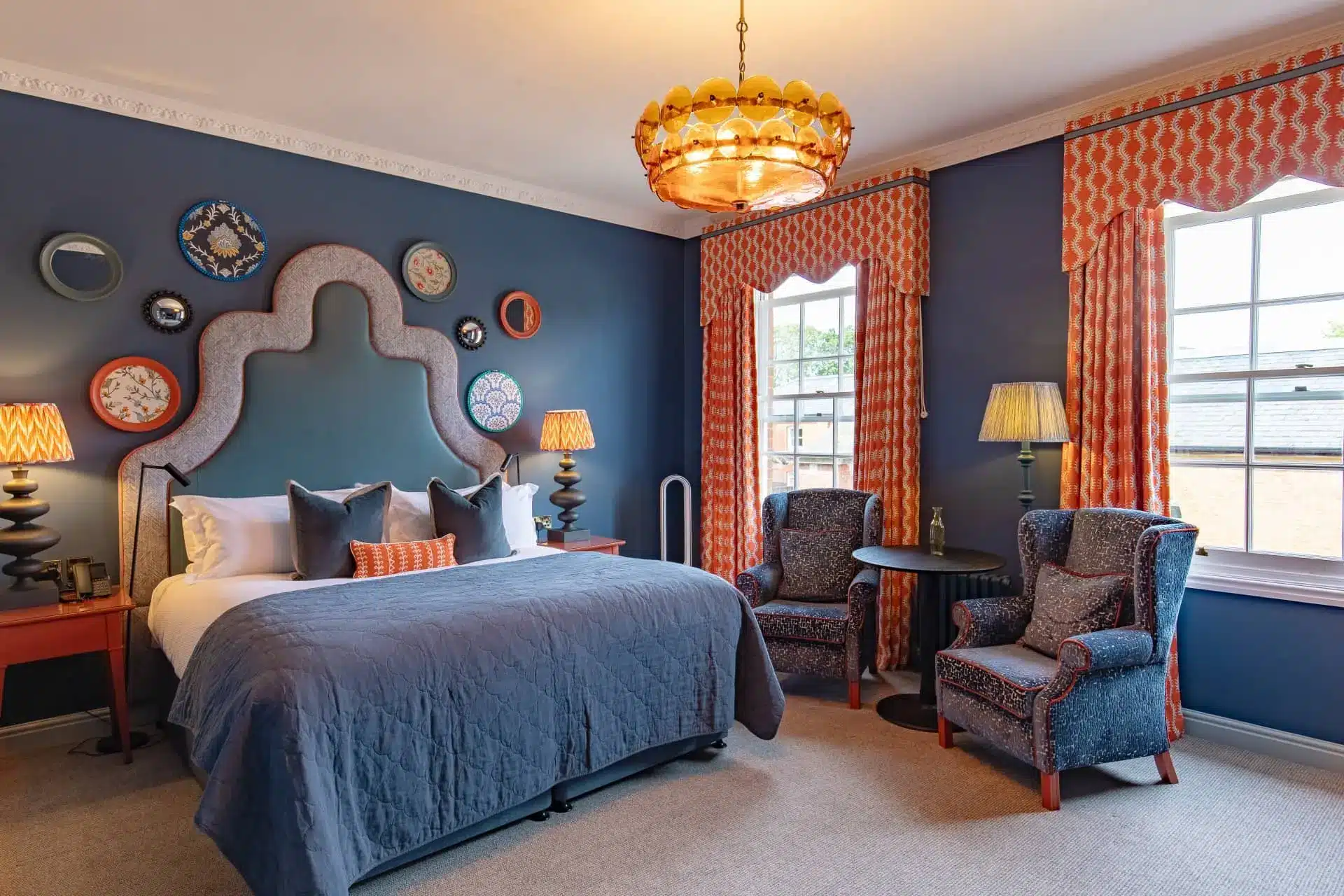 Elegant luxury hotel bedroom with blue walls, patterned curtains, king bed, and ornate chandelier