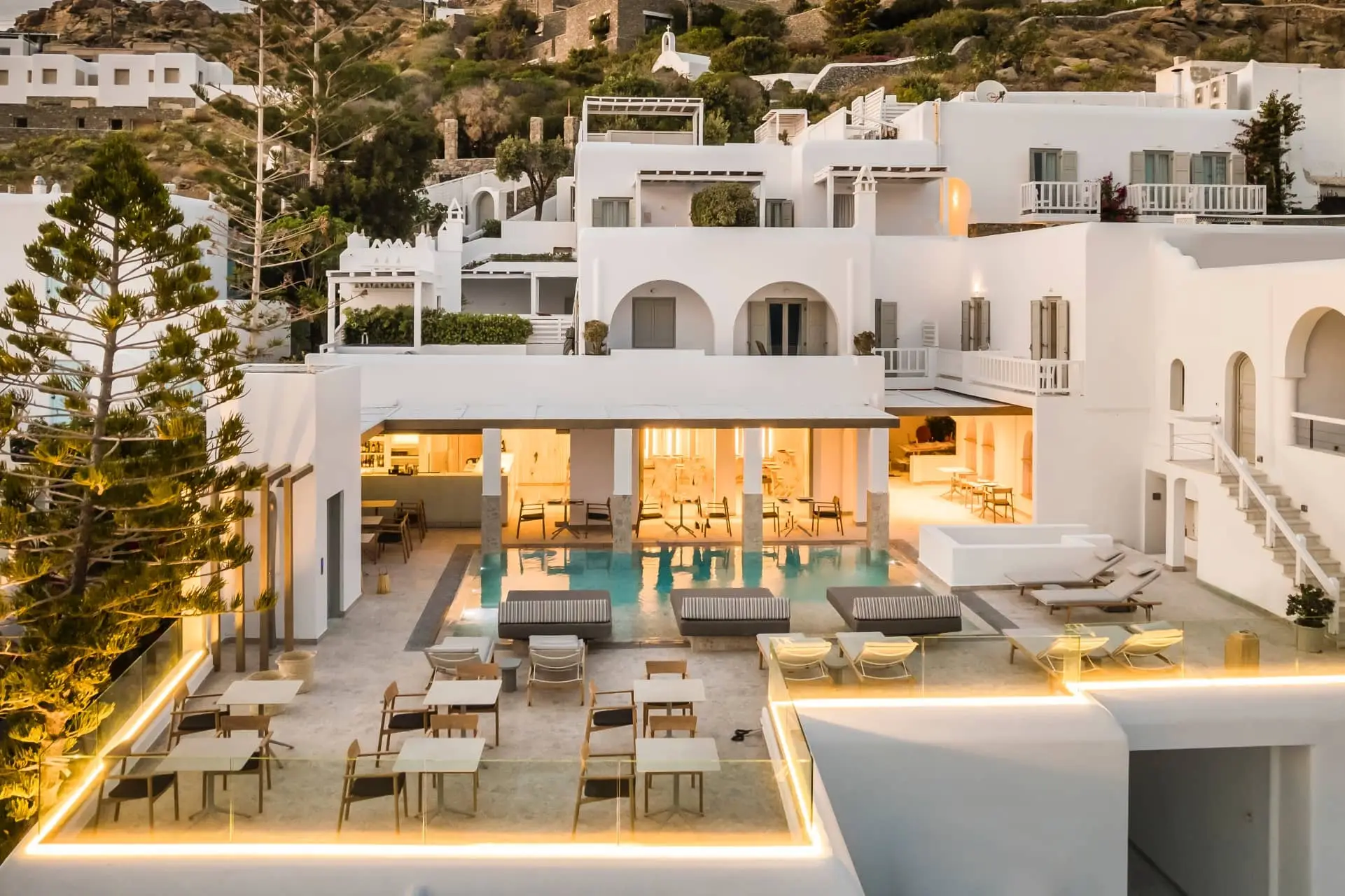 Luxury white hillside villa with a pool, outdoor dining terrace, and glowing evening lights